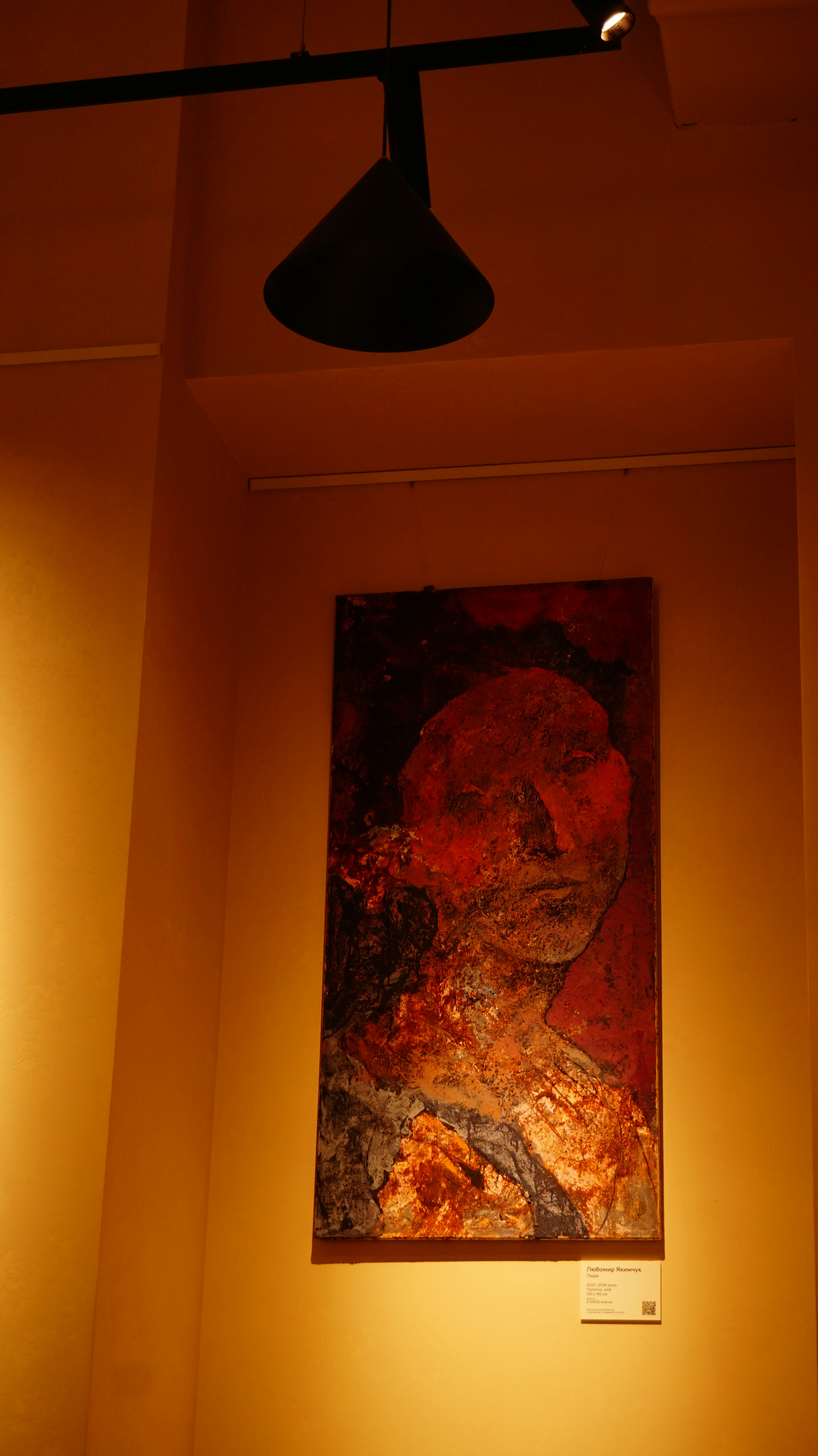 A textured abstract painting of a face in red and brown tones on a wall
