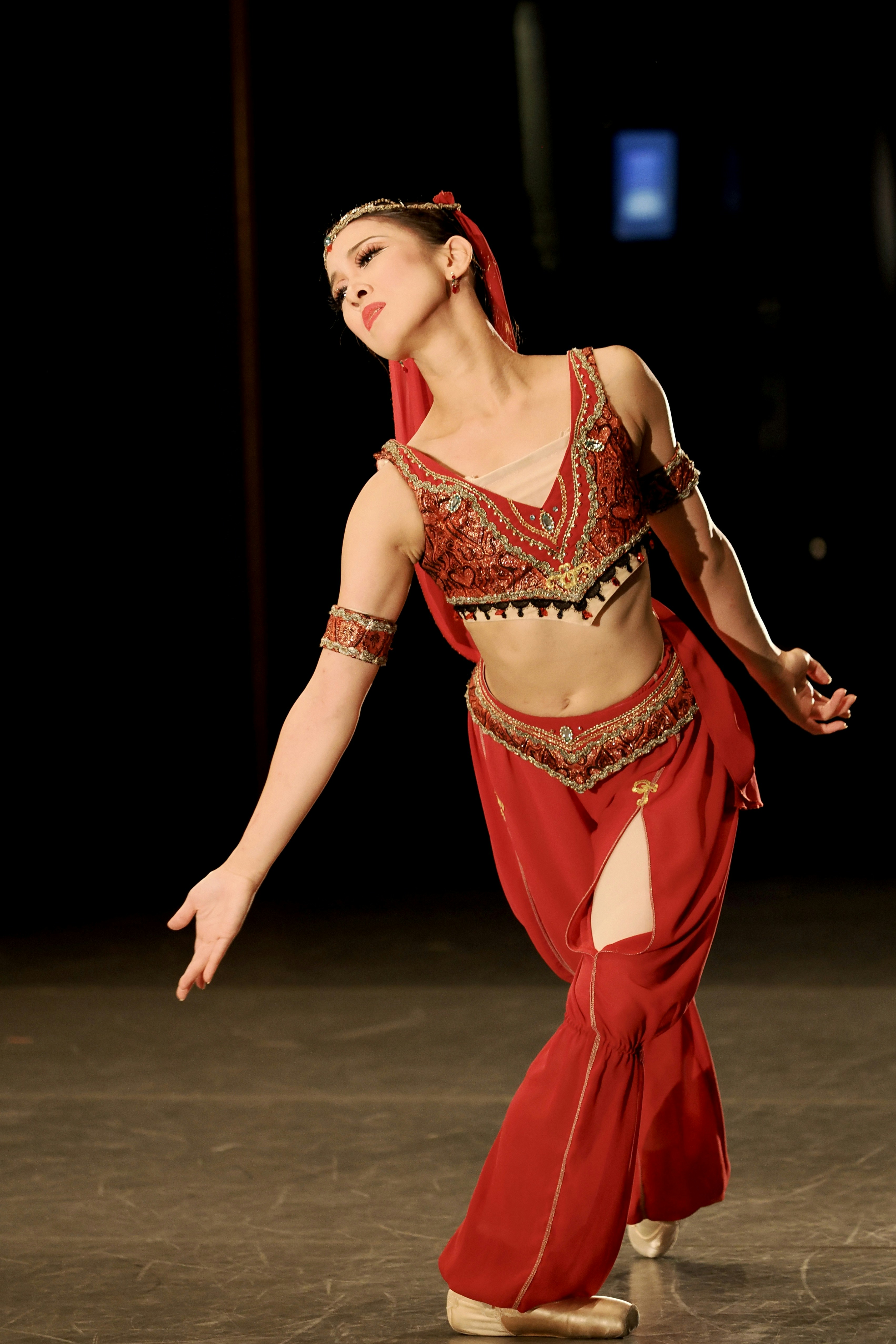 A woman in a red embellished costume dancing on a dark stage