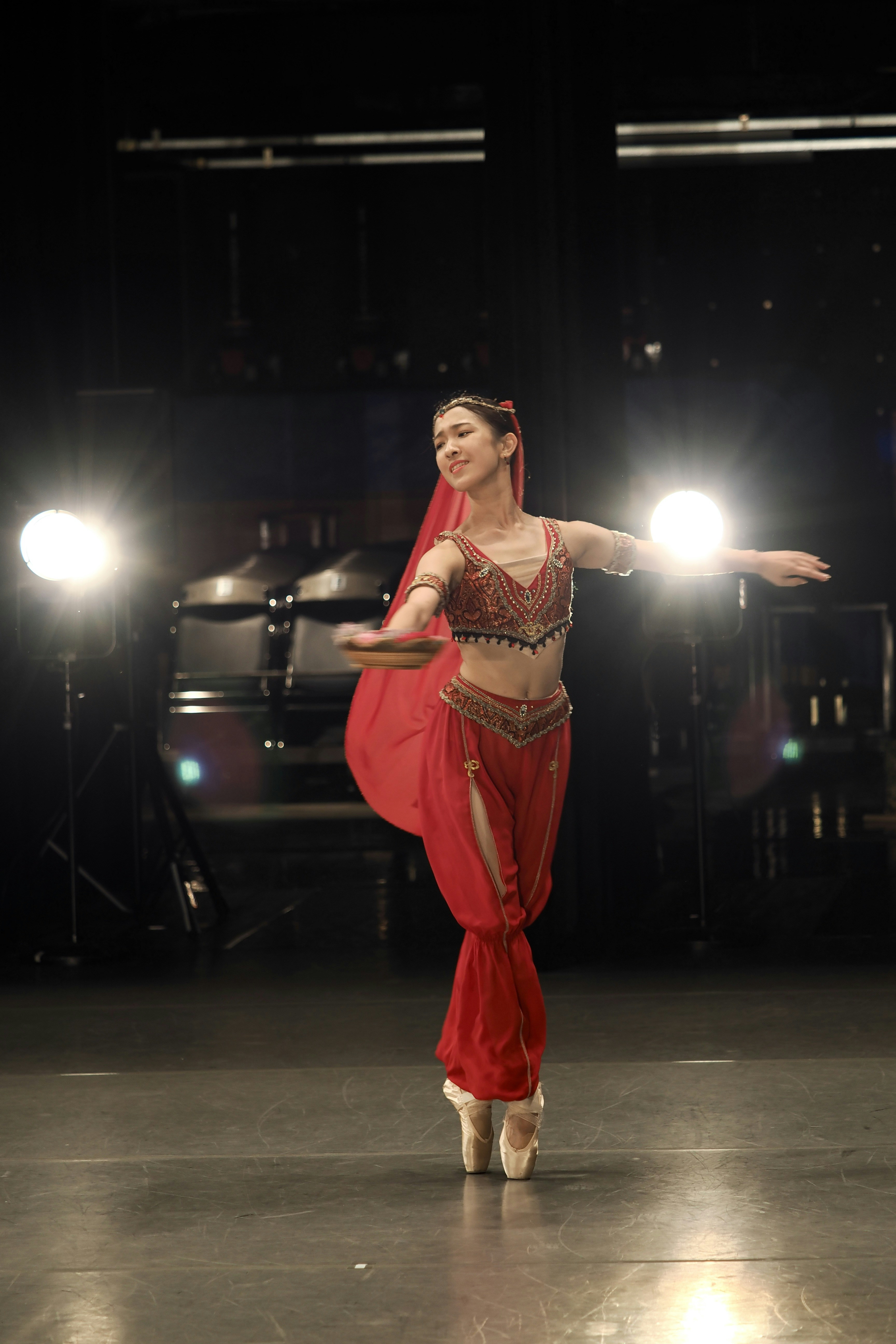 A dancer in a red costume and pointe shoes performing on a stage