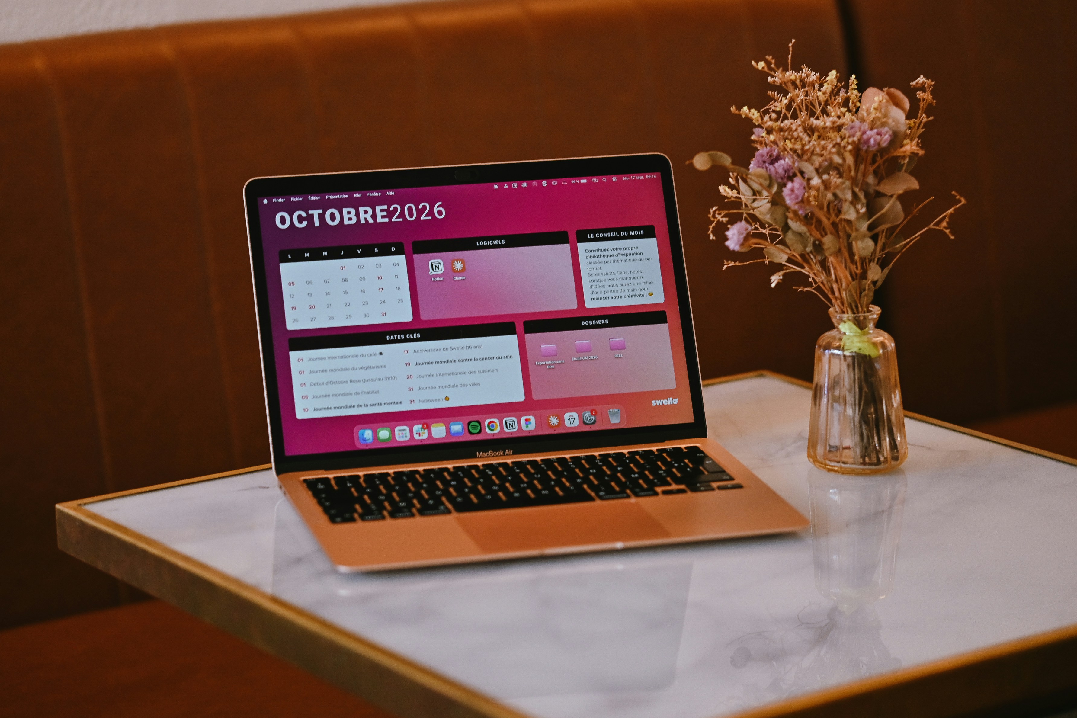 A laptop displaying an October 2026 calendar on a marble table with dried flowers