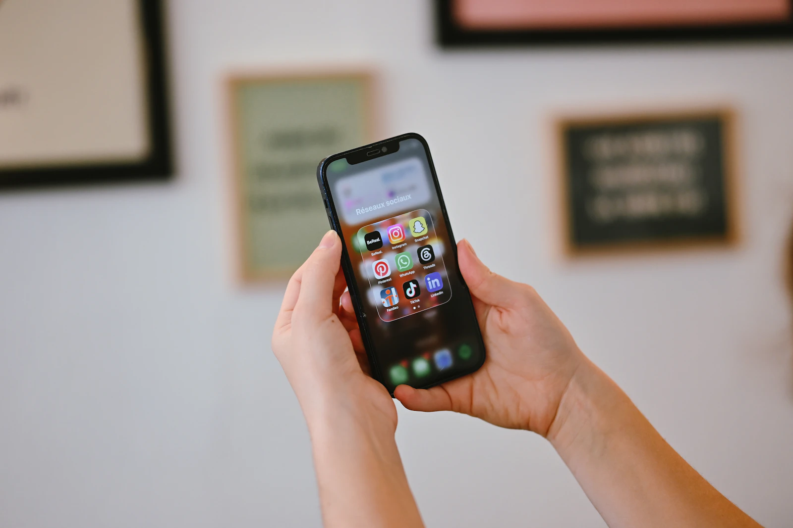 Hands holding a smartphone with a folder of social media app icons on the home screen