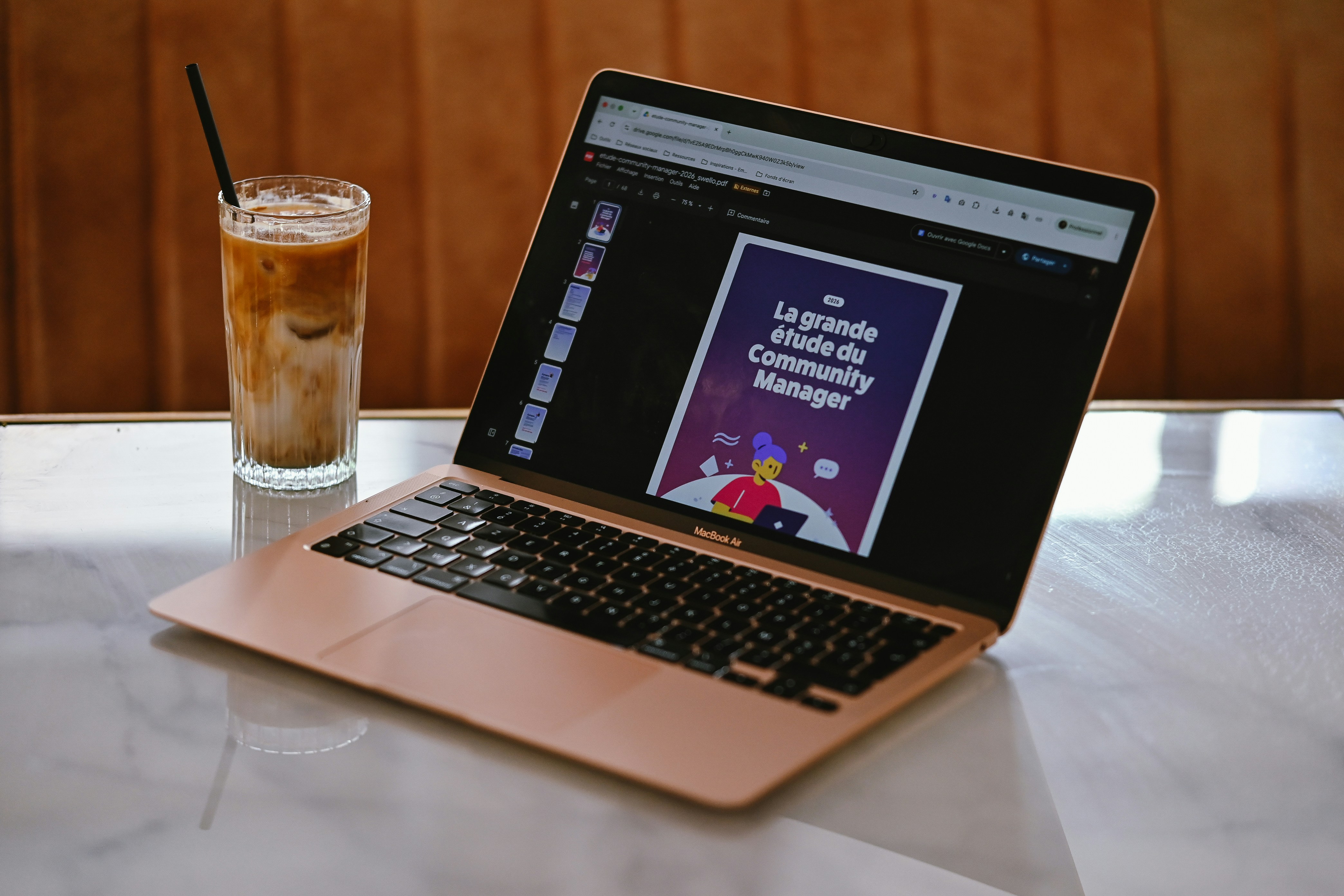 A laptop open on a white marble table next to an iced coffee