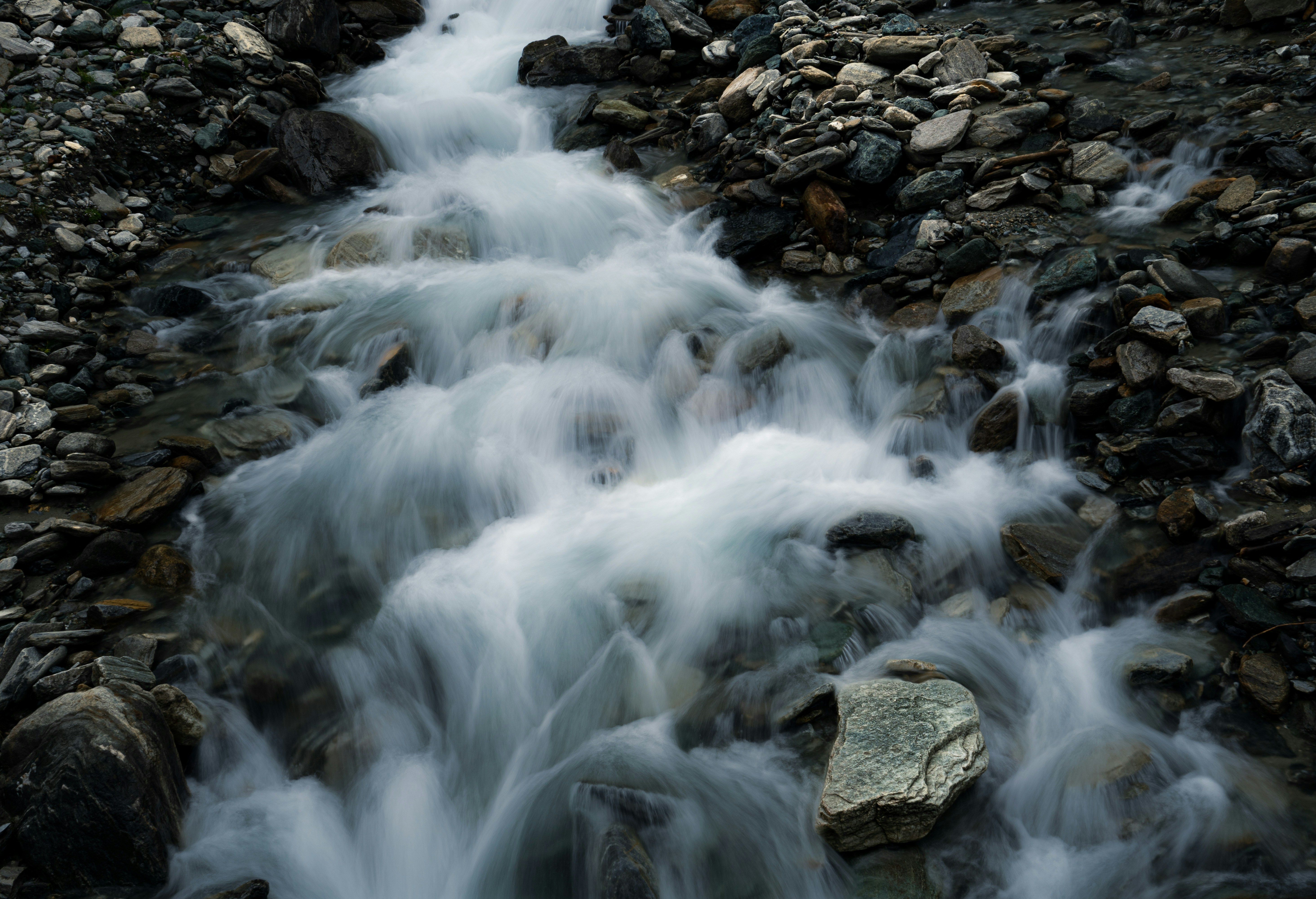 A long exposure of a mountain stream flowing over grey river rocks