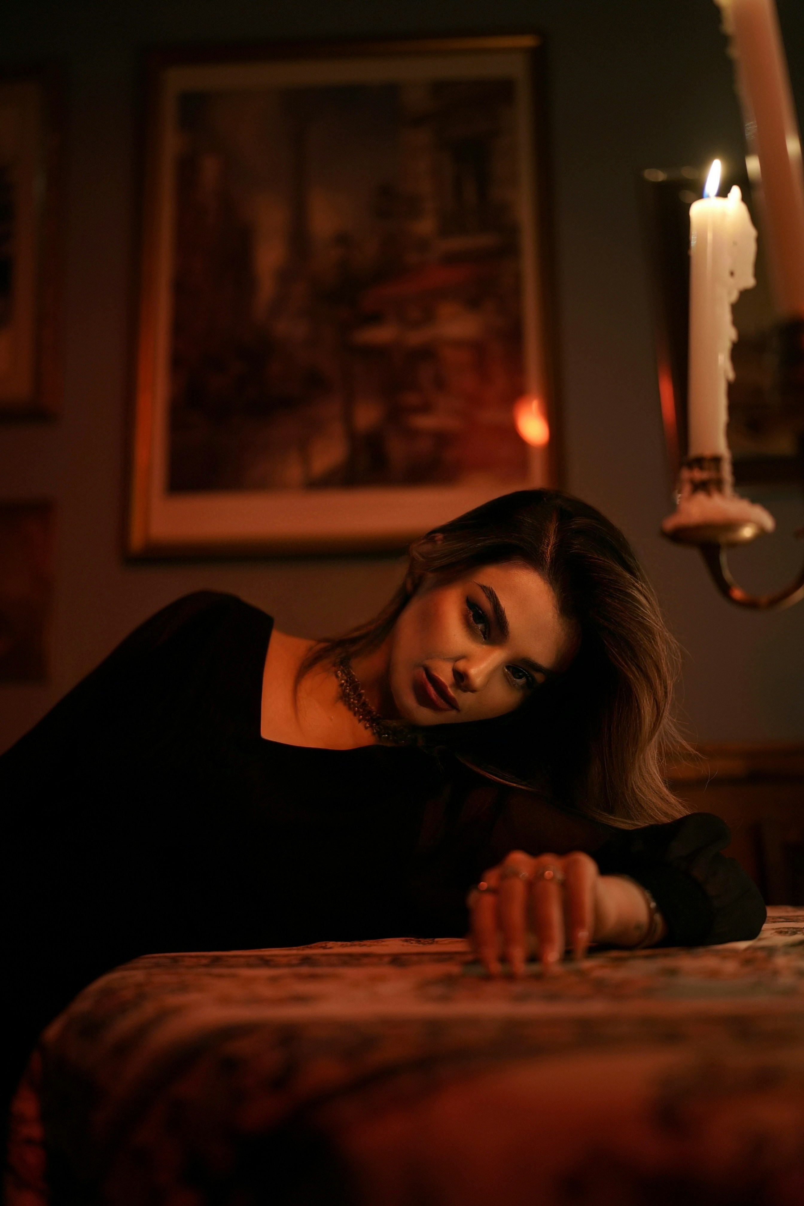 A woman in a black top leaning on a table by candlelight