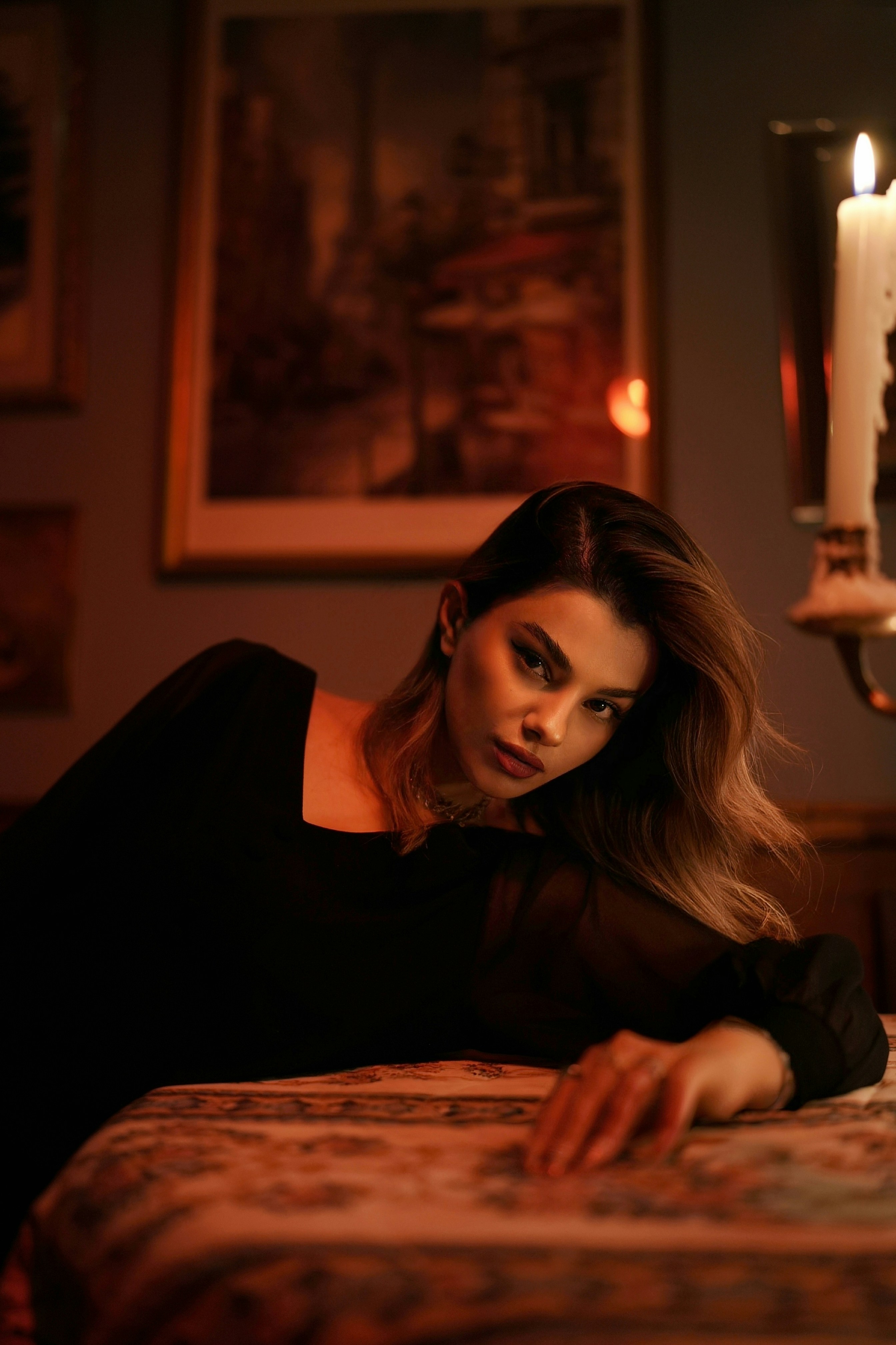 A woman in a black top leaning on a patterned table by candlelight