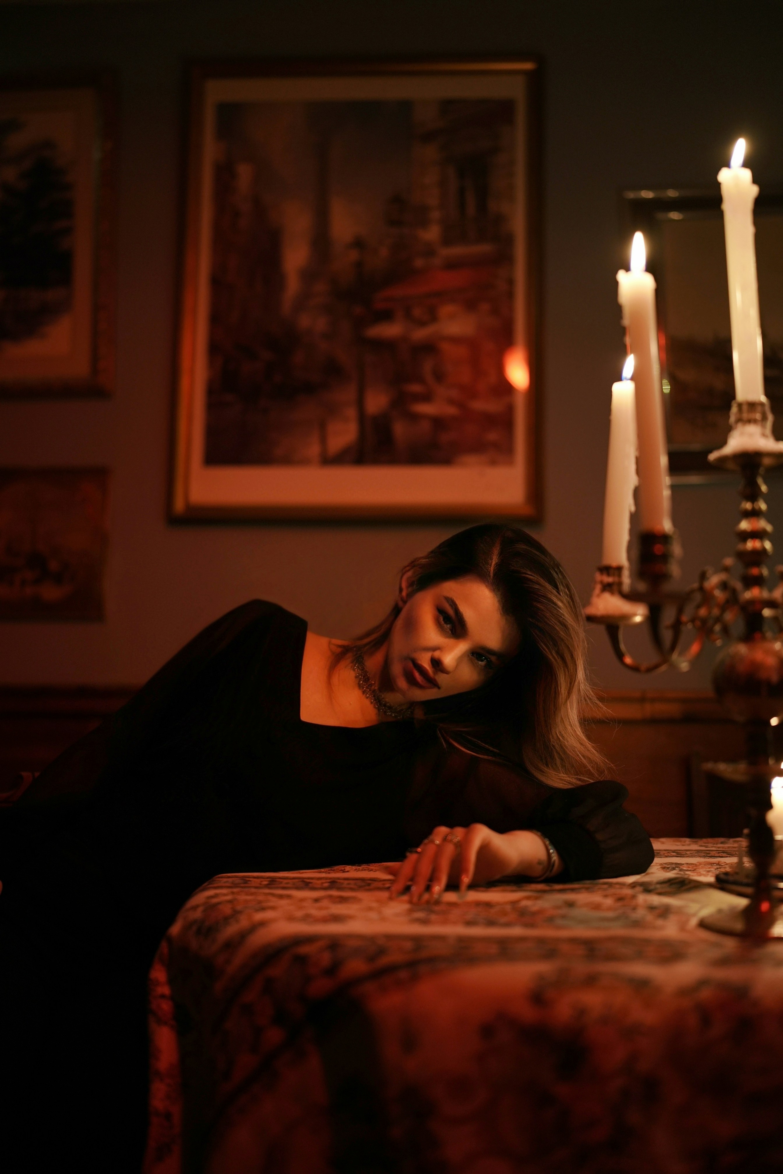 A woman in a black dress leaning on a table beside lit candles