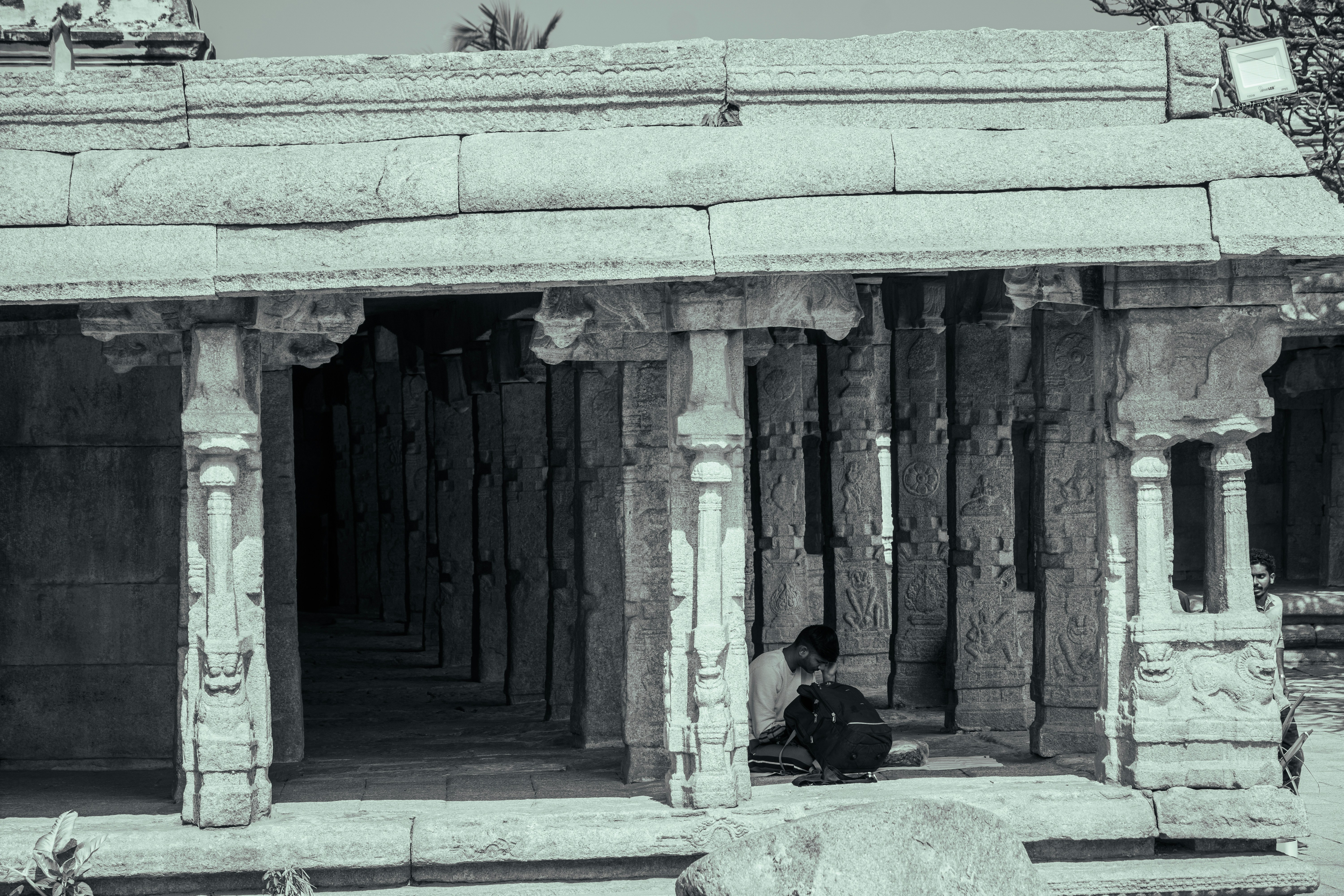 A person sitting with a backpack inside a stone temple with carved pillars