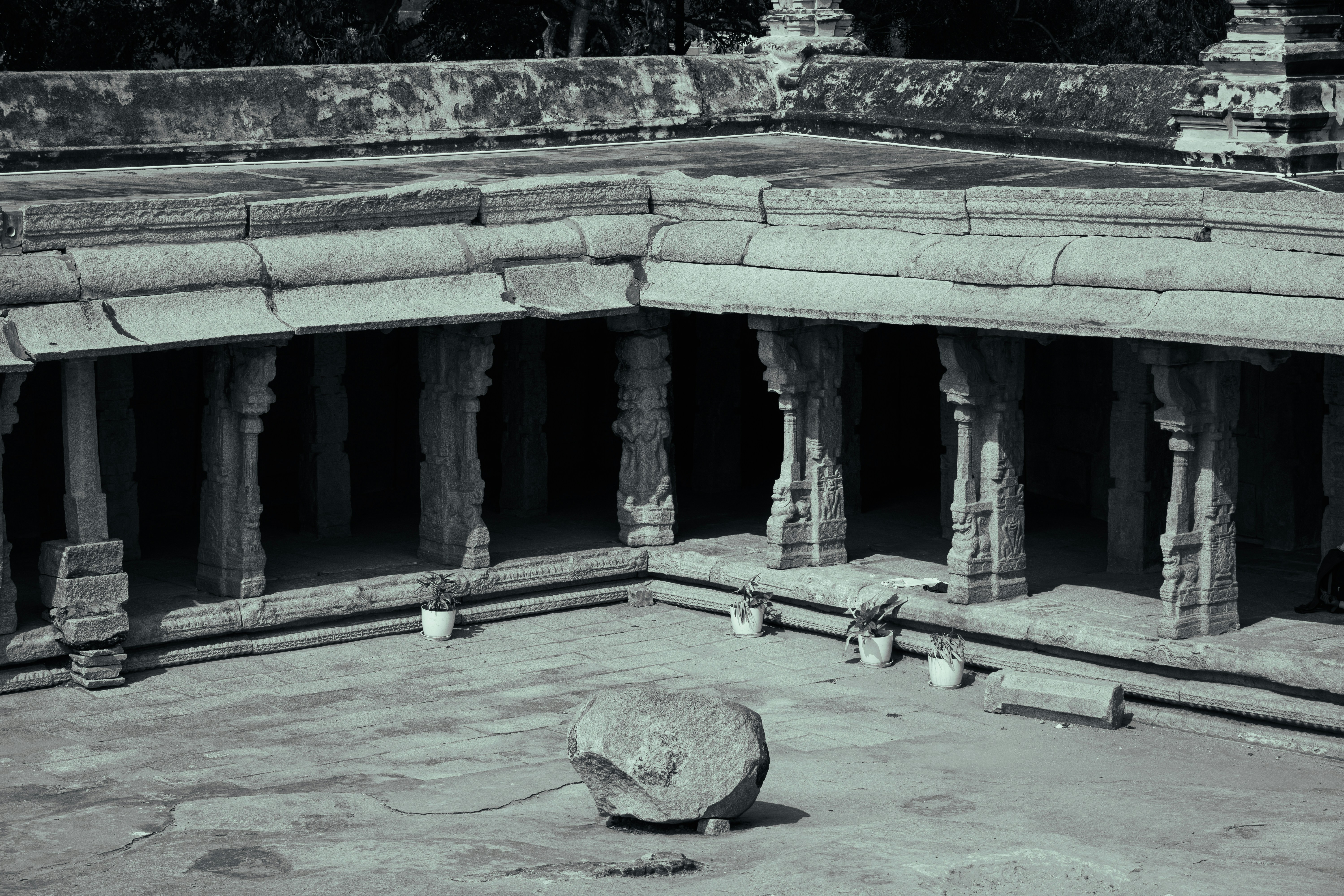 A stone courtyard with carved pillars and potted plants under a roofed walkway