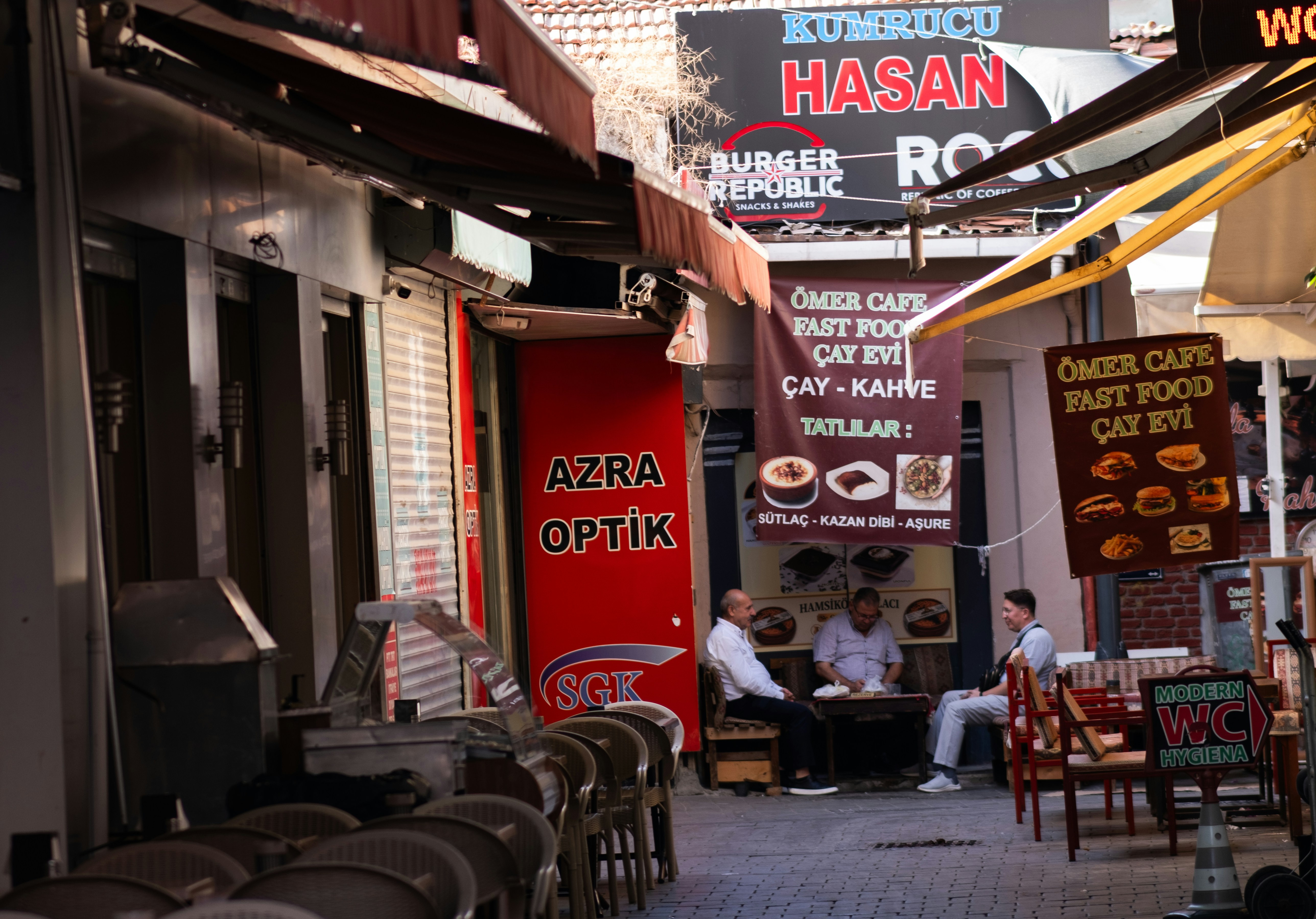 Three men sitting at a small table in a narrow alleyway with shop signs