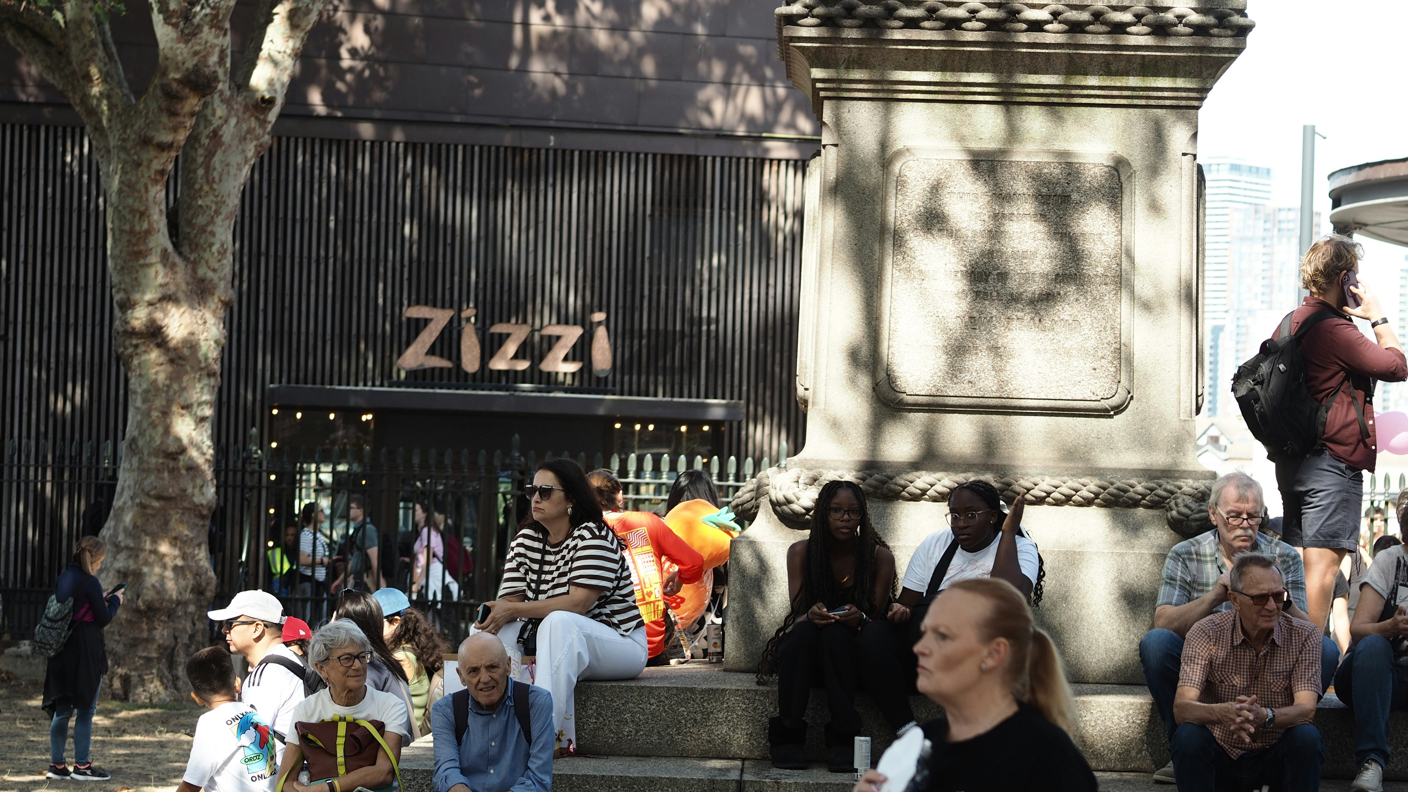 Des gens assis sur des marches en pierre près d’un restaurant Zizzi et d’un grand monument