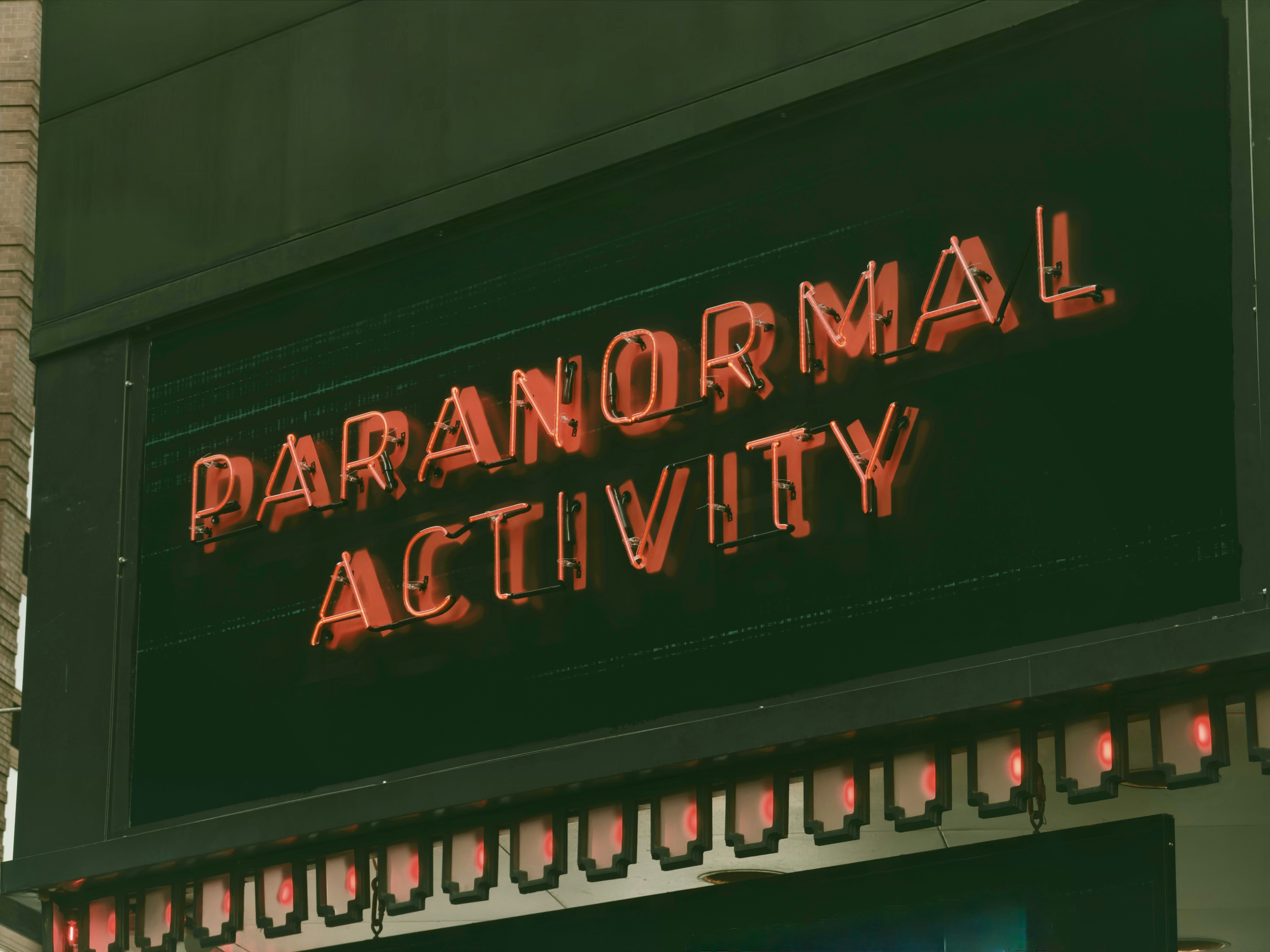 A red neon sign reading "PARANORMAL ACTIVITY" on a dark building facade