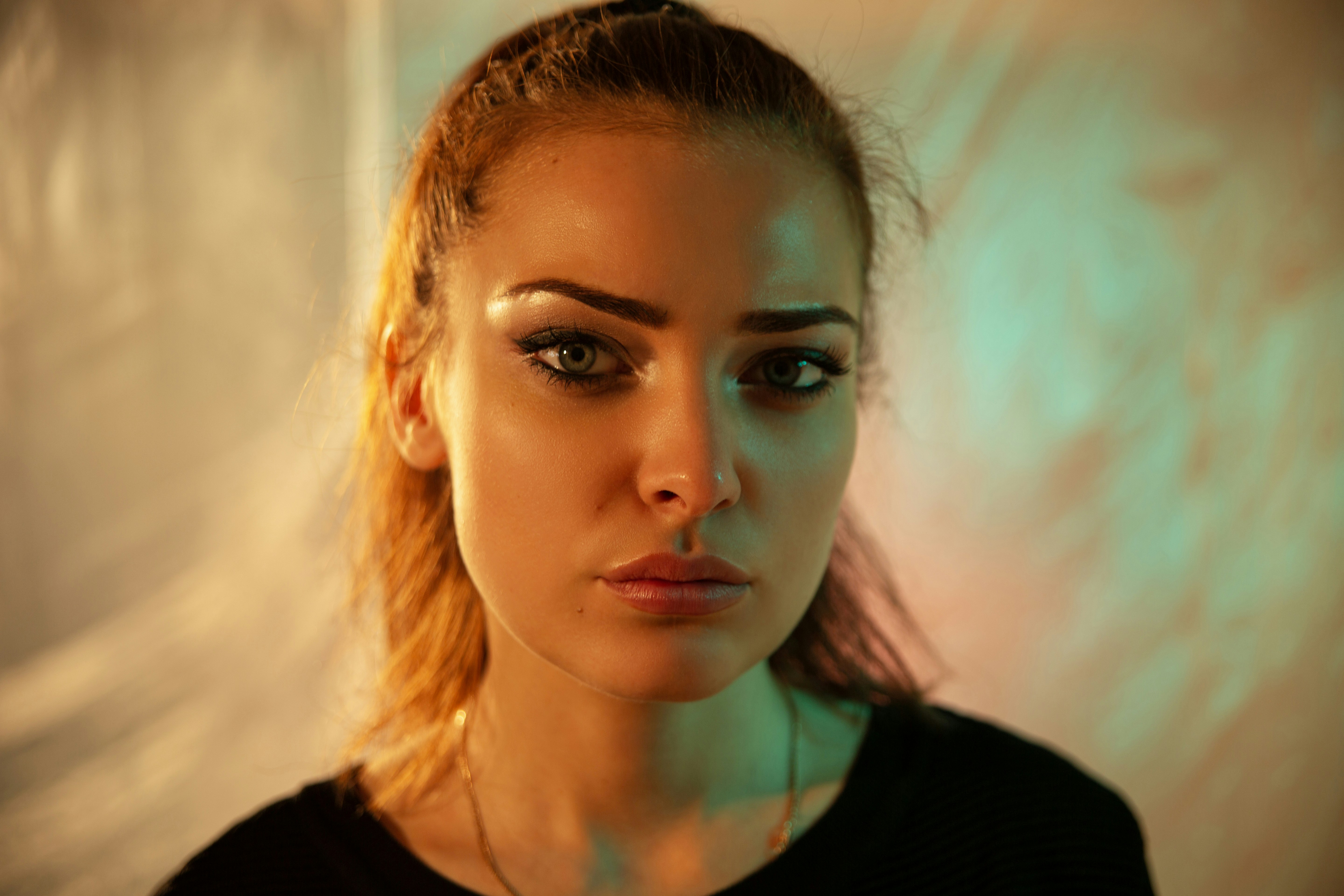 A woman with hair pulled back in a black shirt under orange and green light