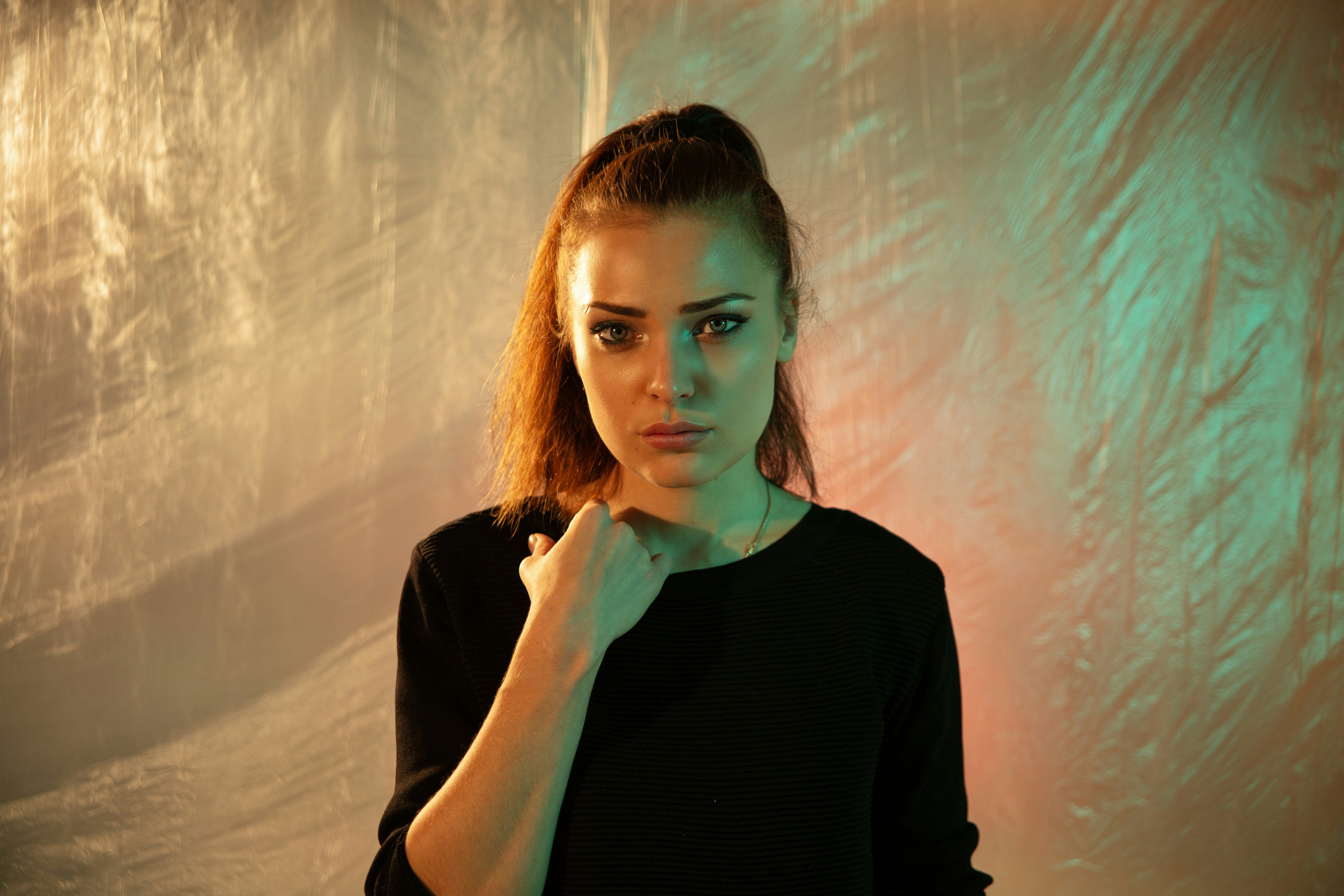 A woman in a black shirt against a crinkled background with orange and green light