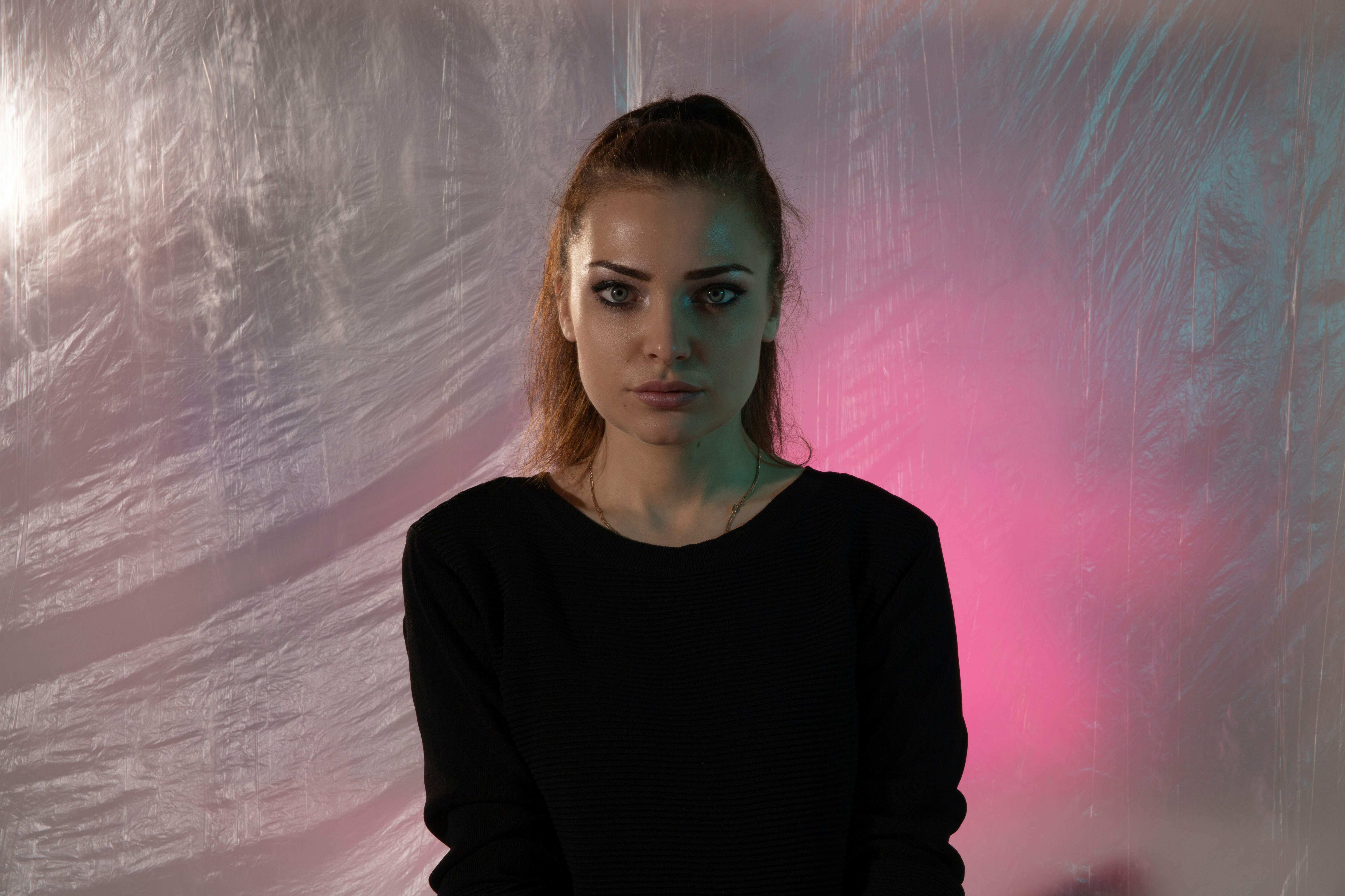 A woman in a black shirt against a crinkled plastic background with pink light