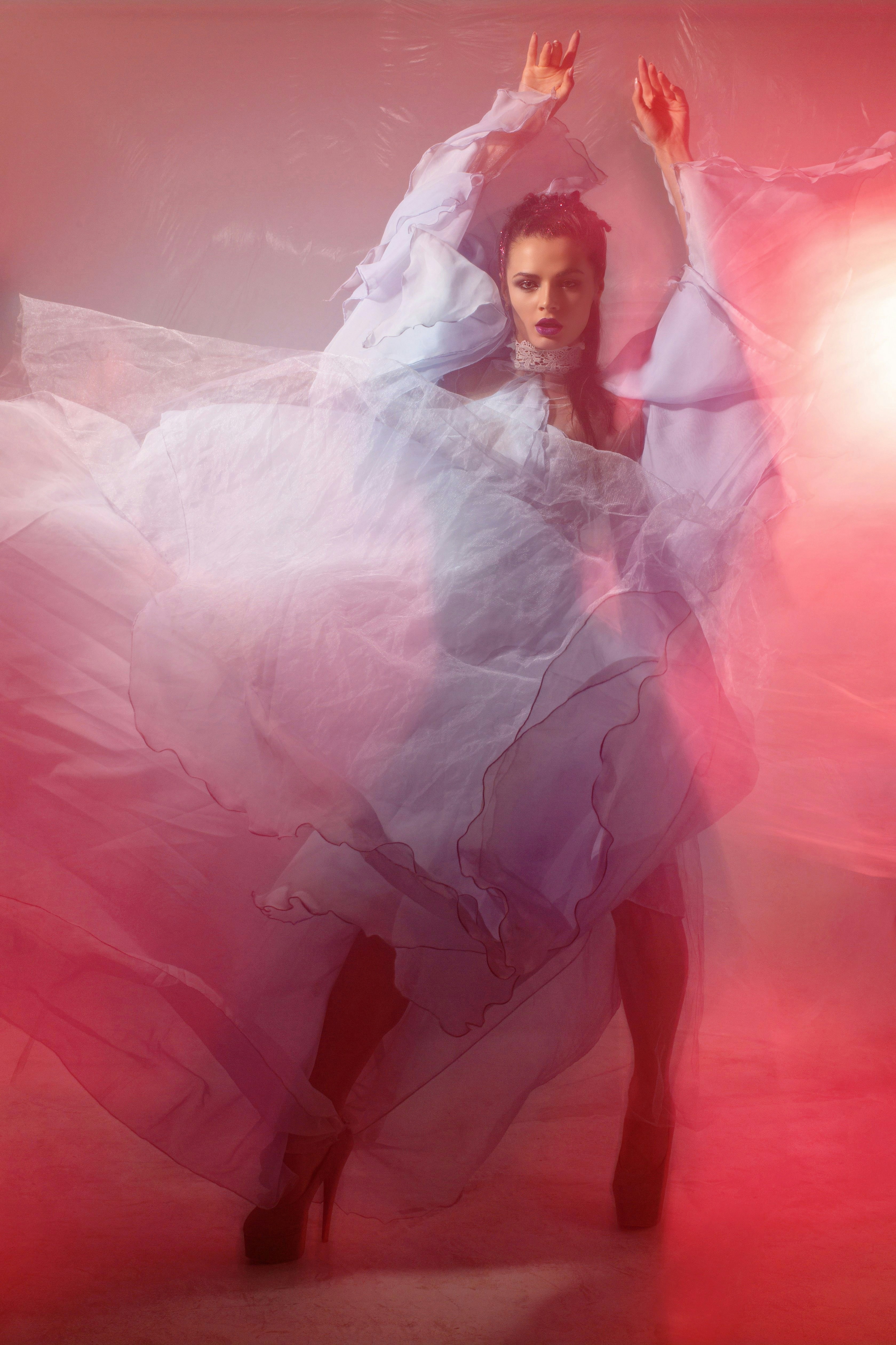 A woman in a flowing light blue dress dancing under red and pink light