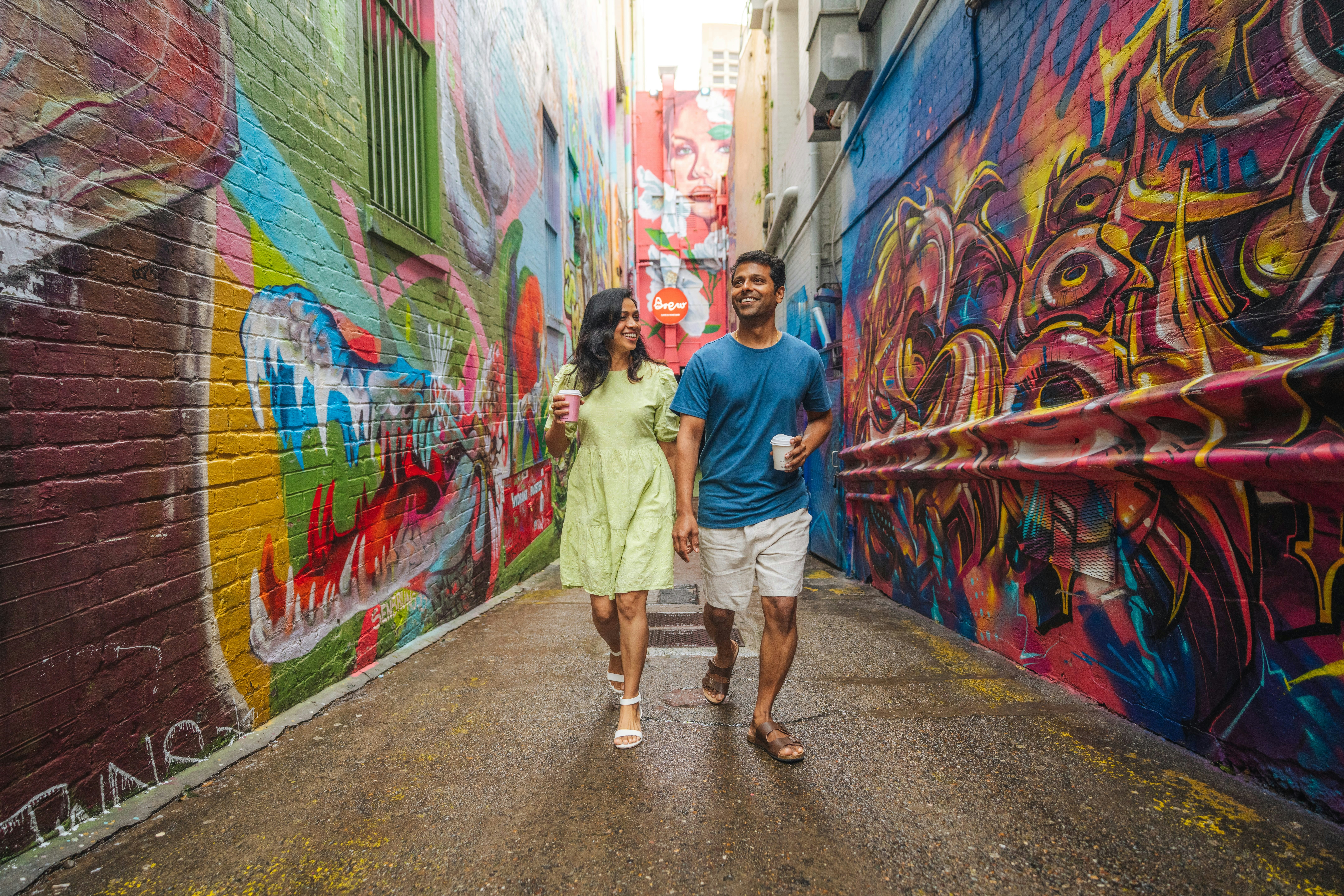 A woman and a man walking through a narrow alleyway with colorful graffiti walls
