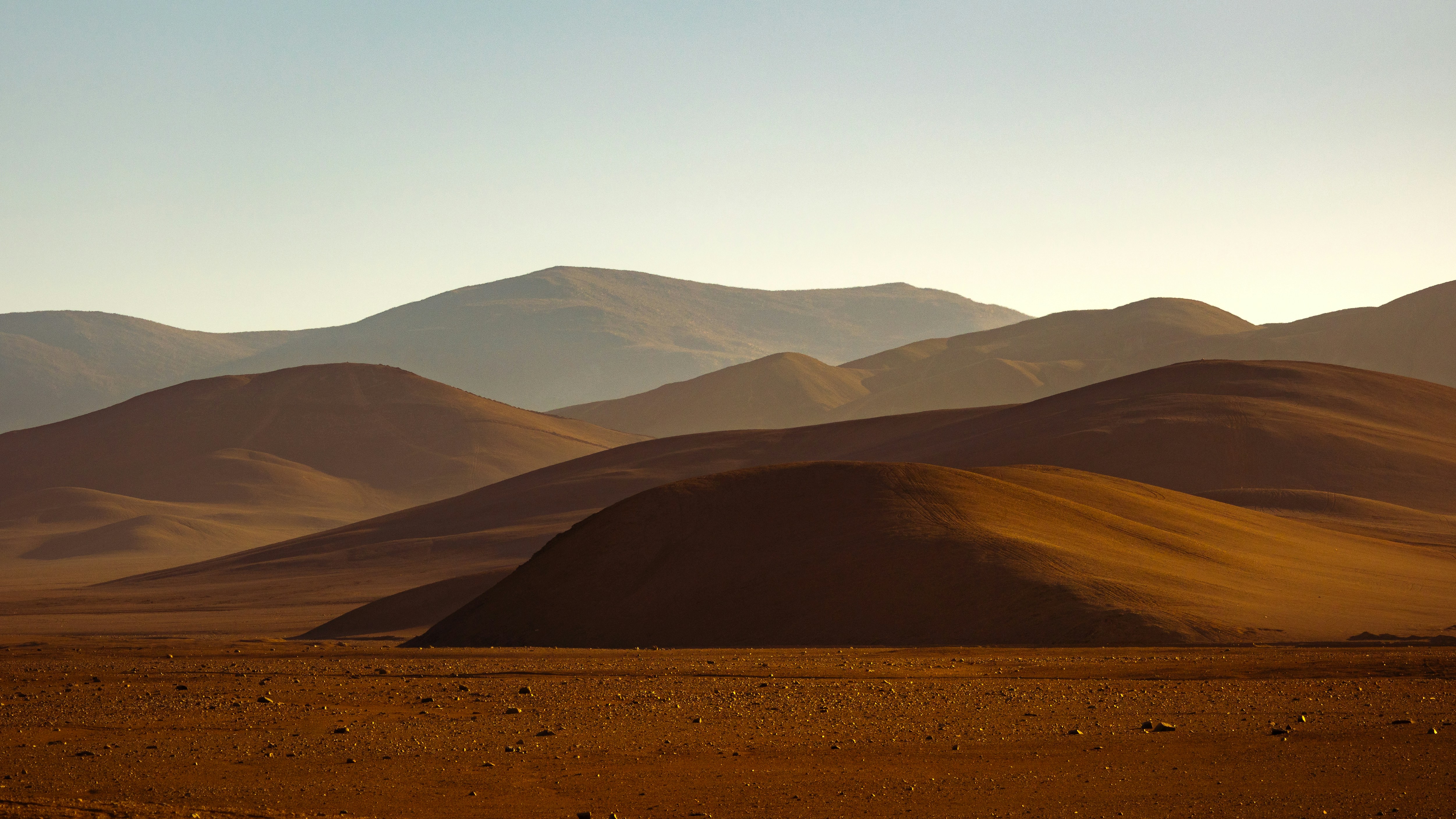Layered brown desert hills under a clear sky during the golden hour