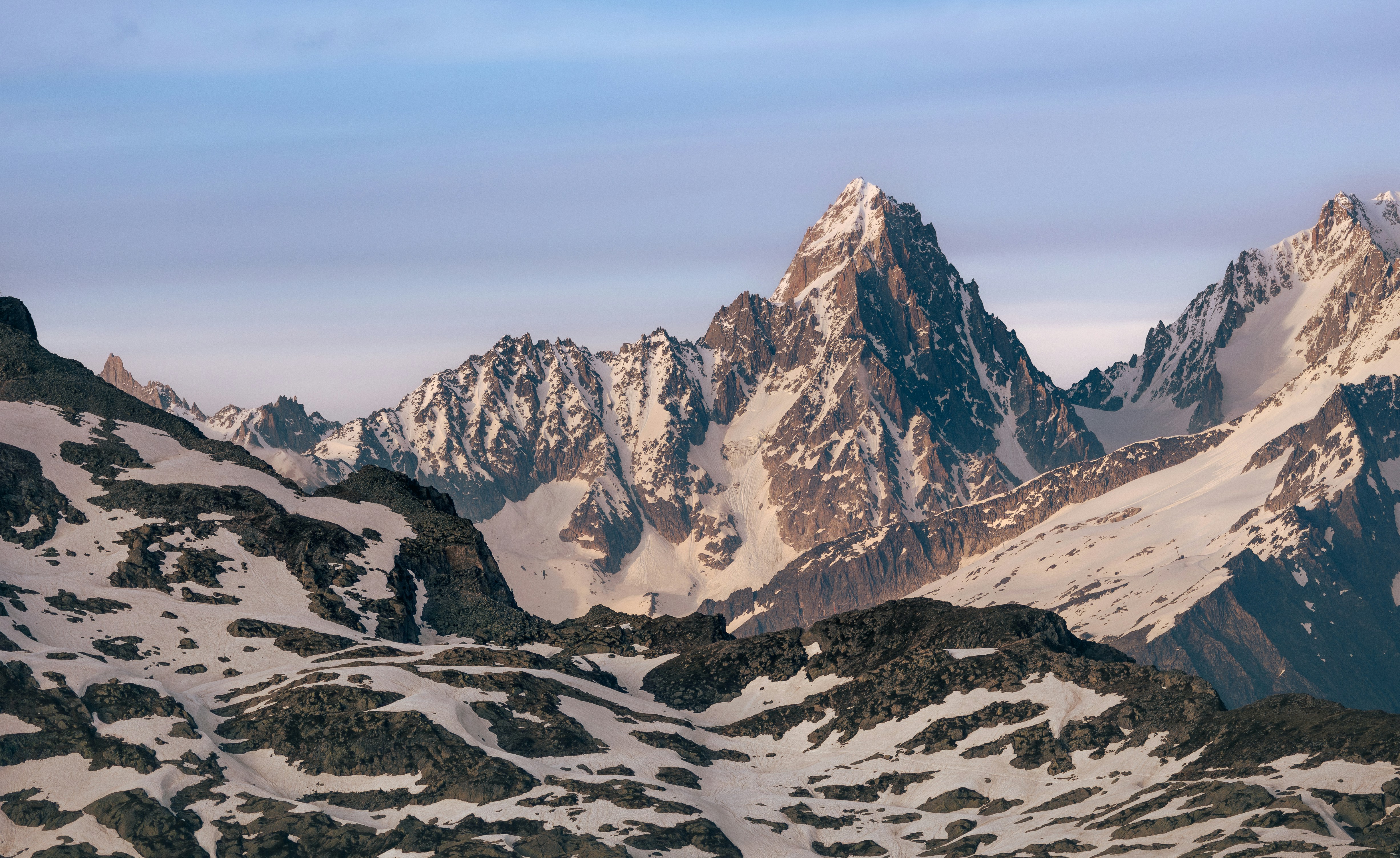 Snow-covered jagged mountain peaks under a pale blue sky with soft light