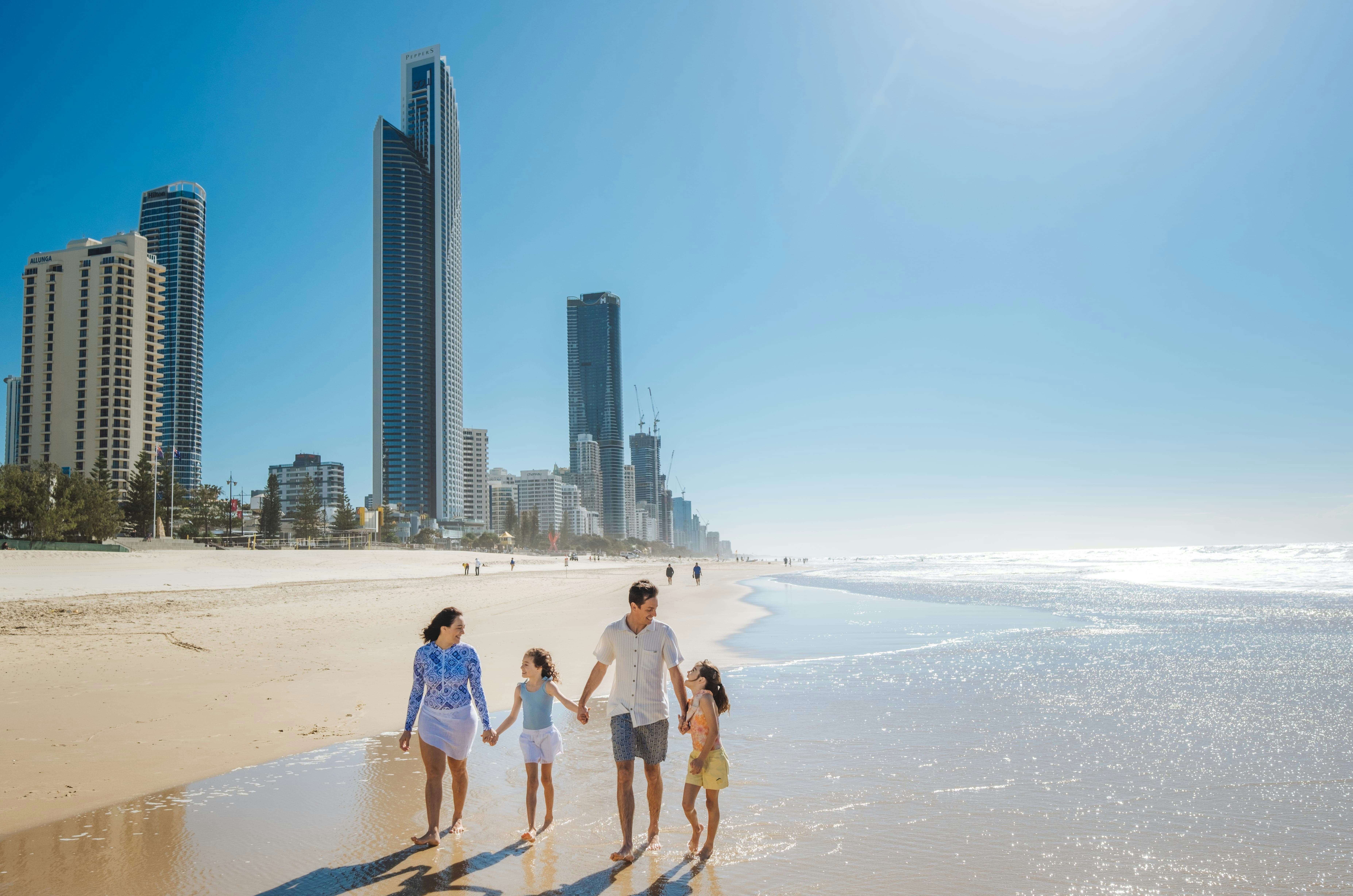 A family walking along the sandy beach in Surfers Paradise with city skyscrapers