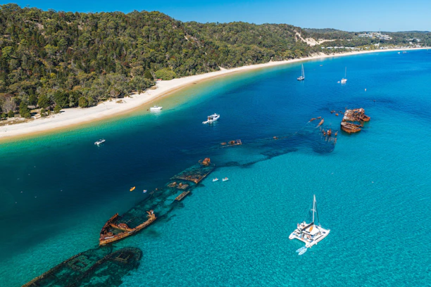 Aerial view of rusted shipwrecks in turquoise water near a sandy beach in Moreton Island