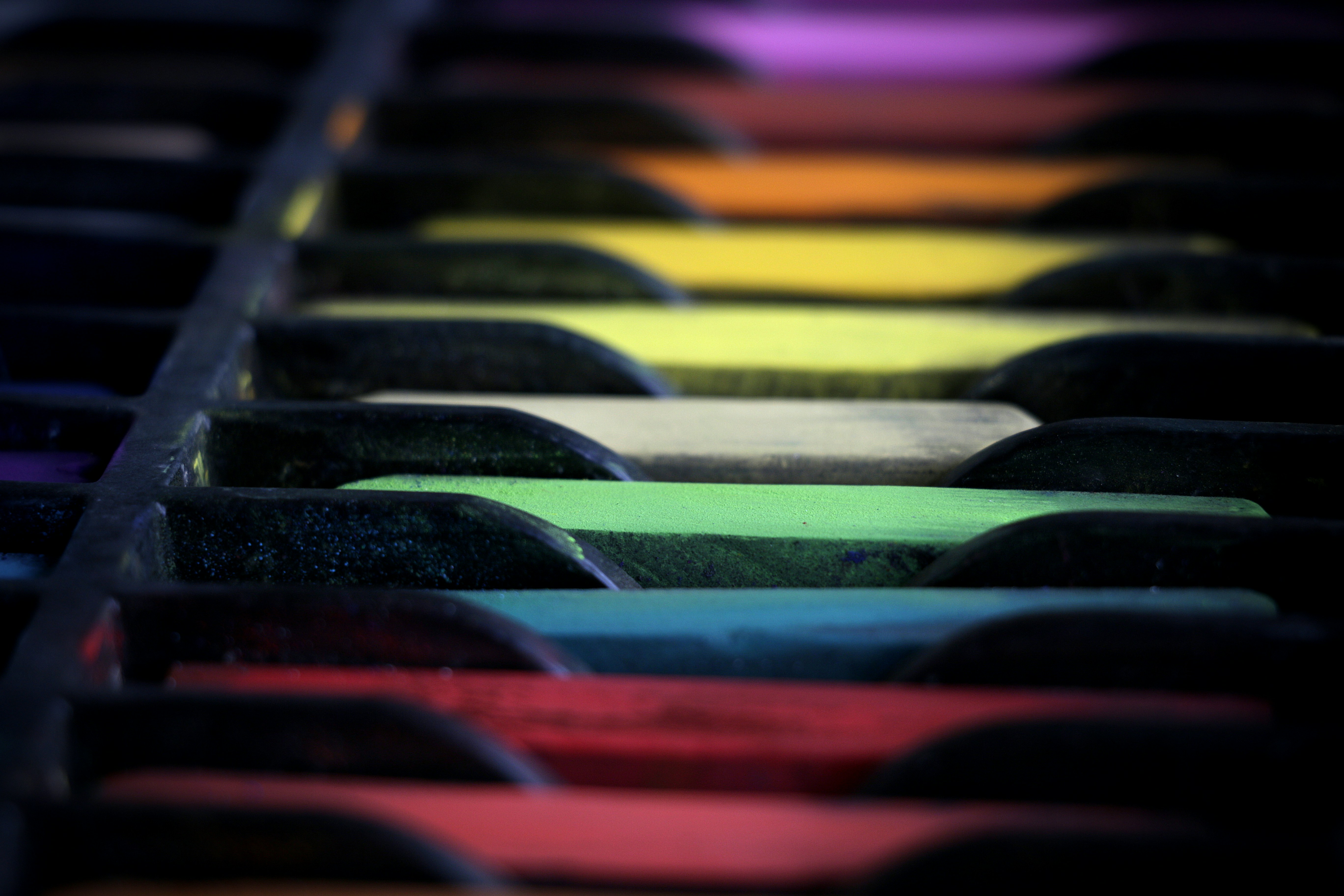 A row of colorful rectangular pastel sticks arranged in a dark partitioned tray