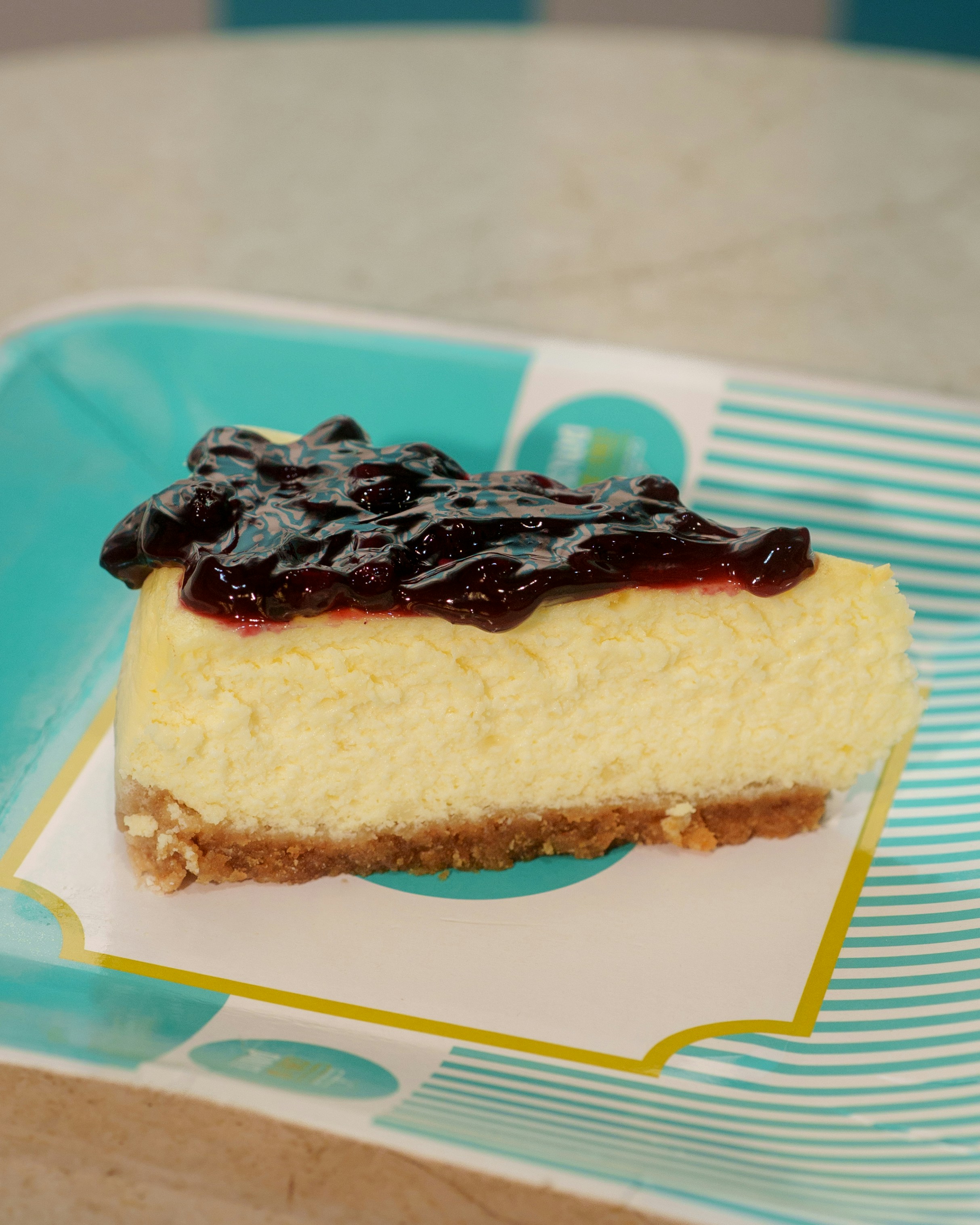 A slice of cheesecake with blueberry topping on a striped paper plate