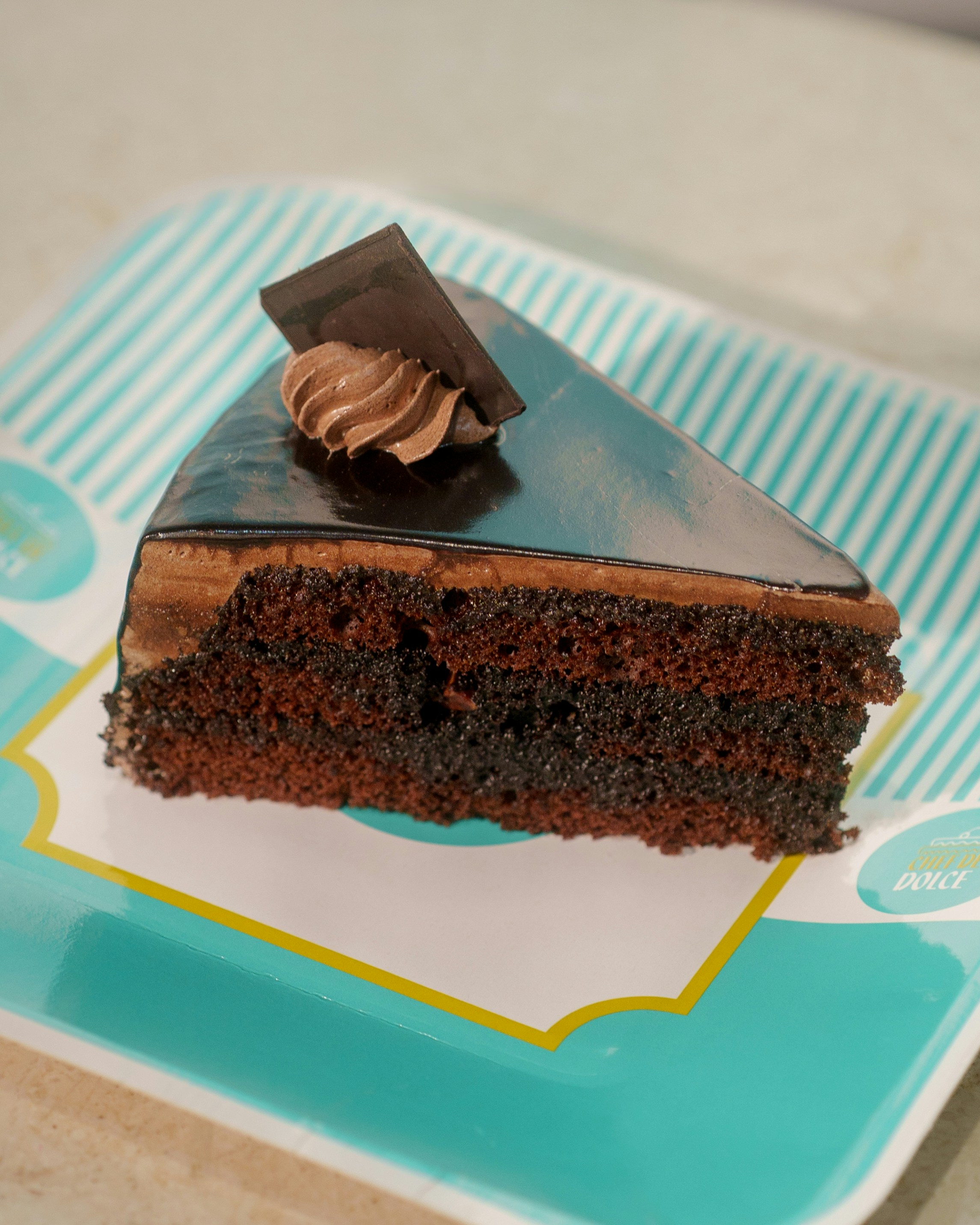 A slice of layered chocolate cake with chocolate glaze on a patterned plate