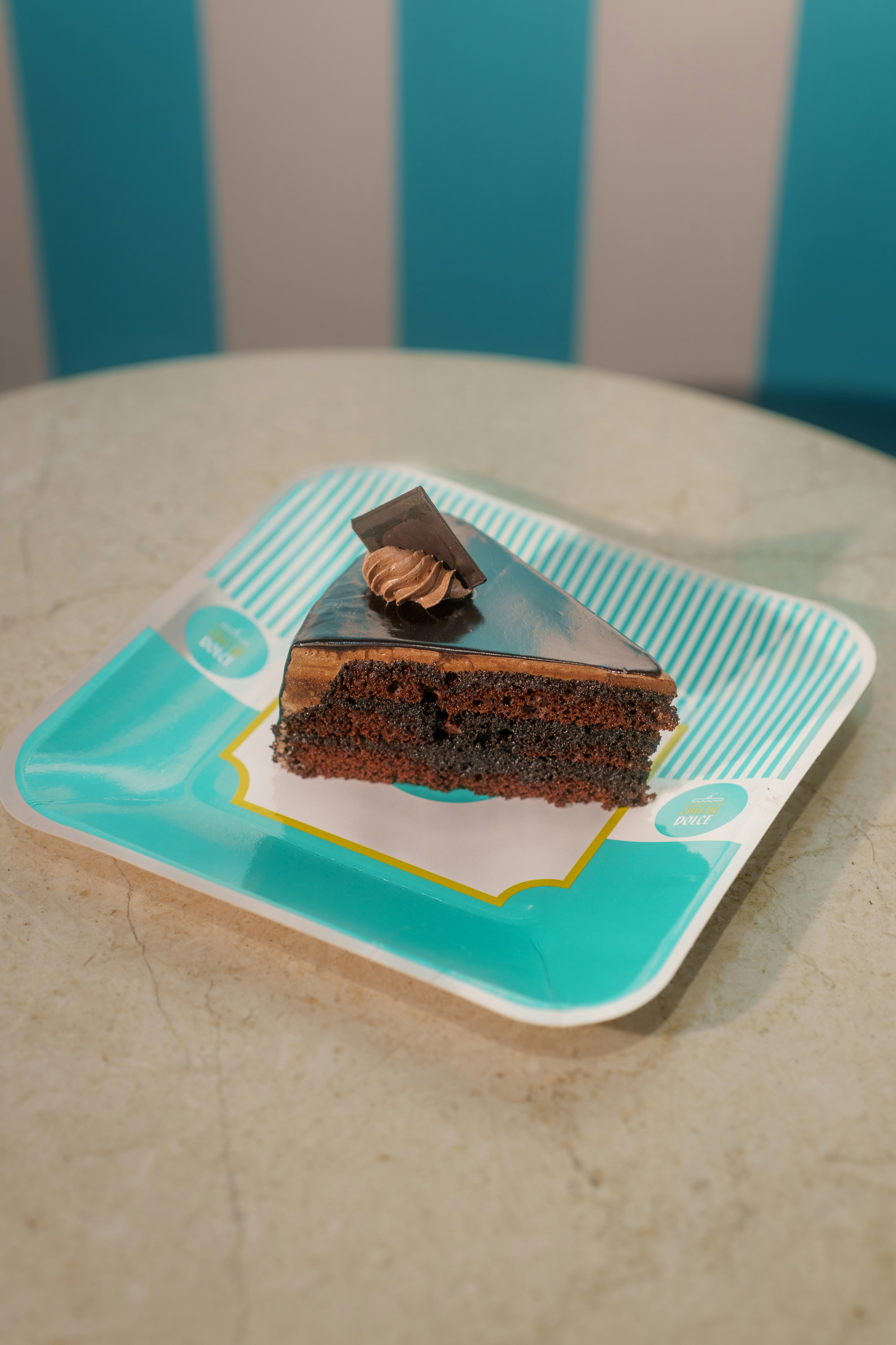 A slice of chocolate cake on a patterned turquoise plate on a table