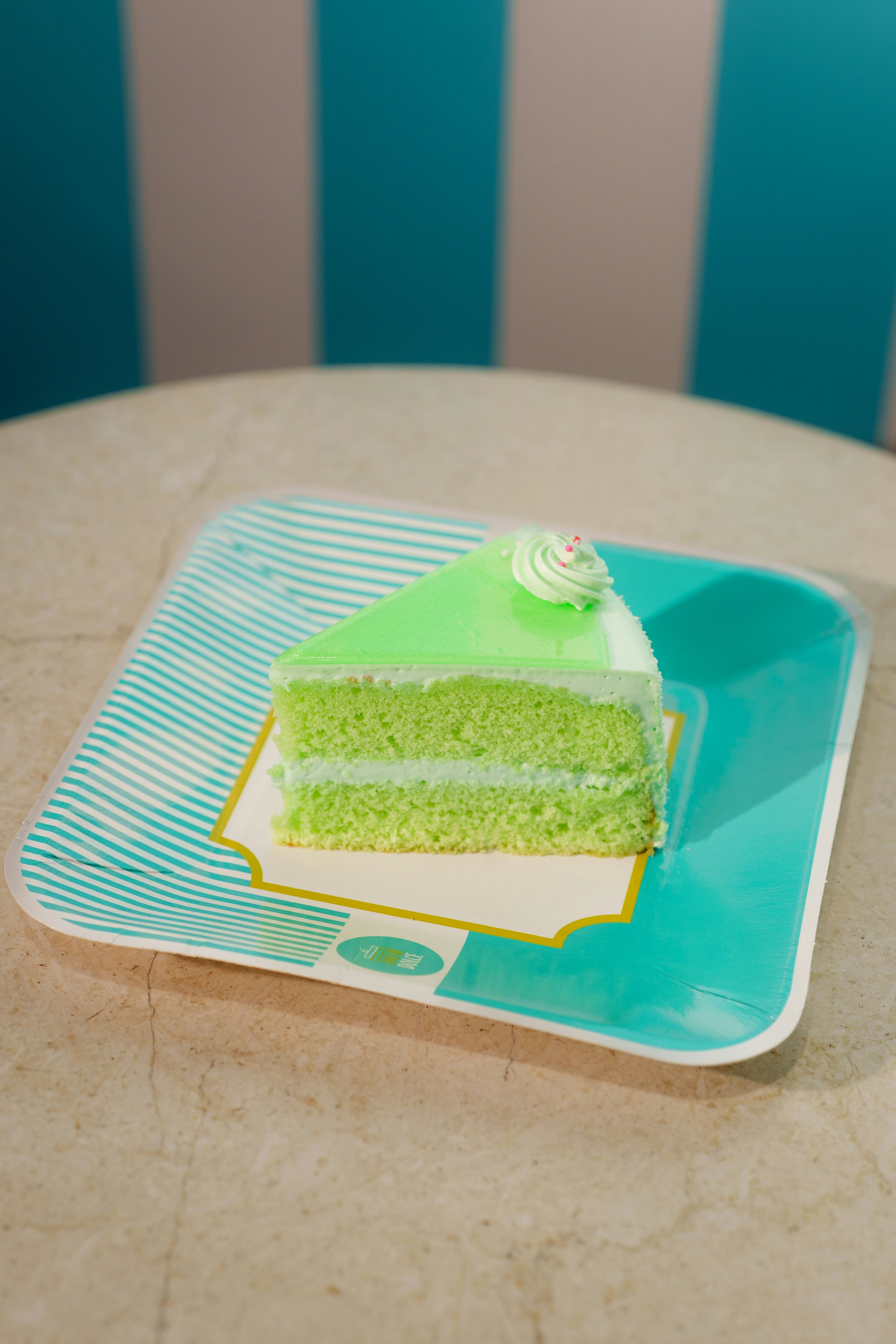 A slice of green cake with frosting on a patterned paper plate