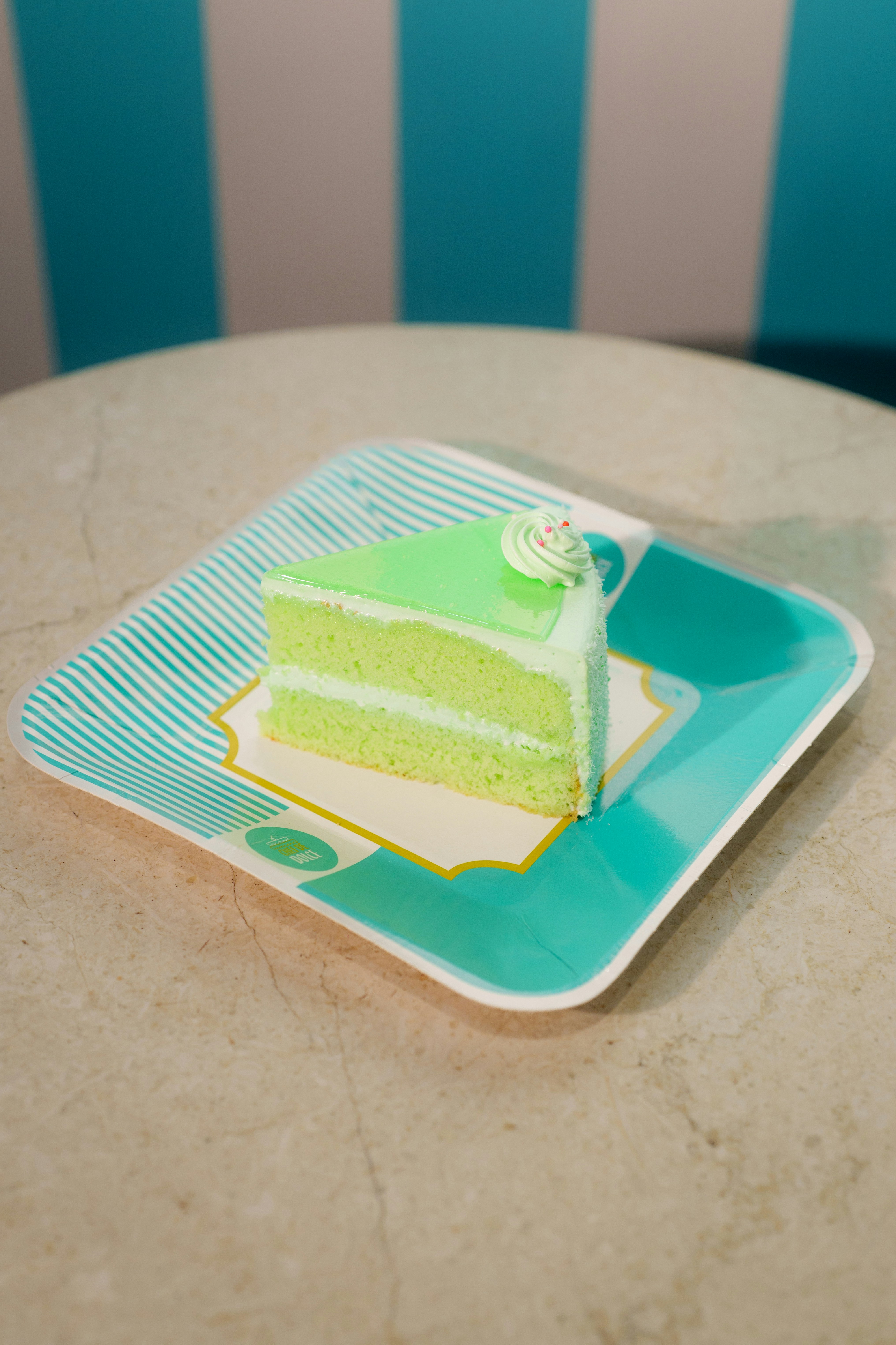 A slice of green cake on a teal paper plate