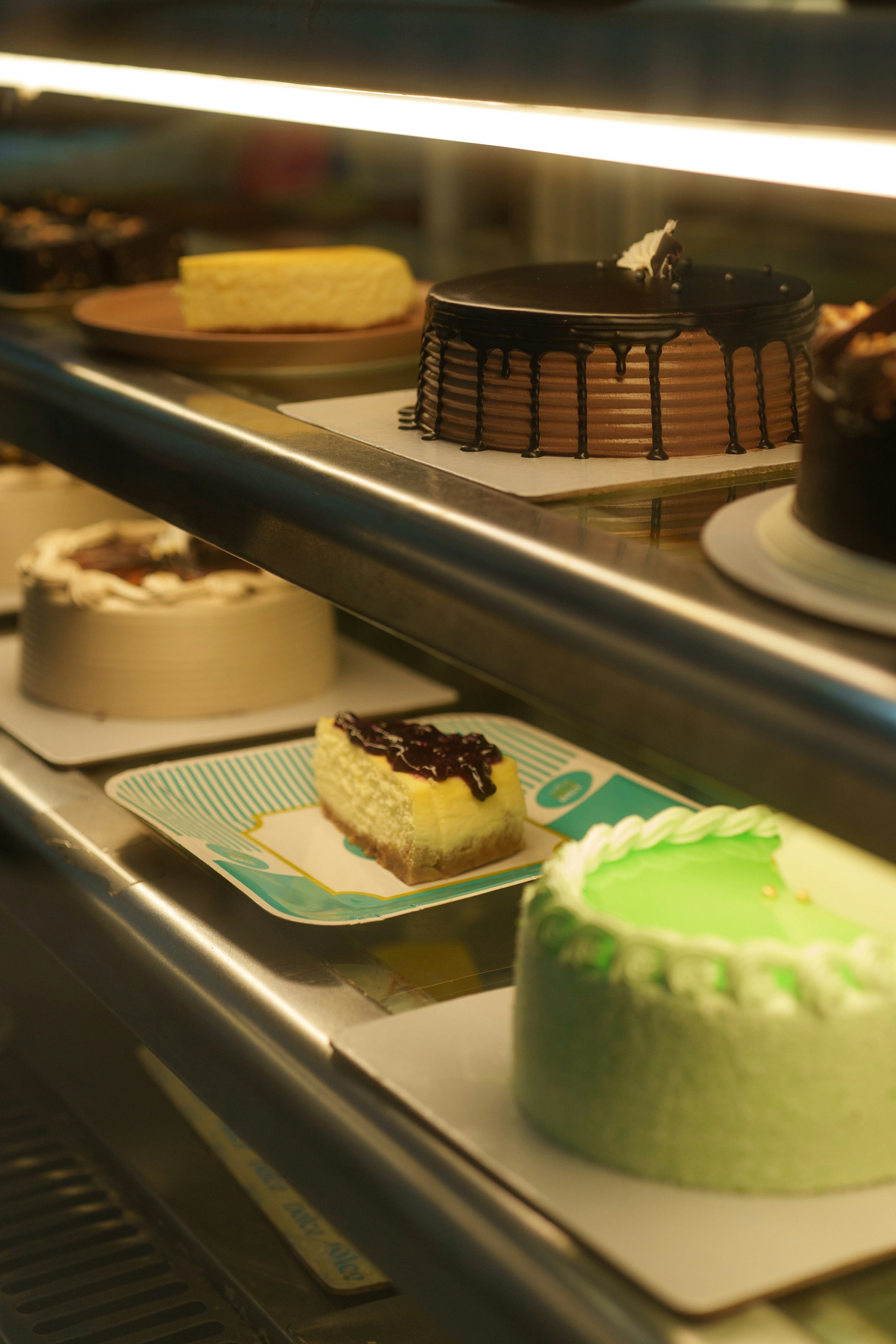 Assorted cakes and cheesecake slices on illuminated shelves in a bakery display