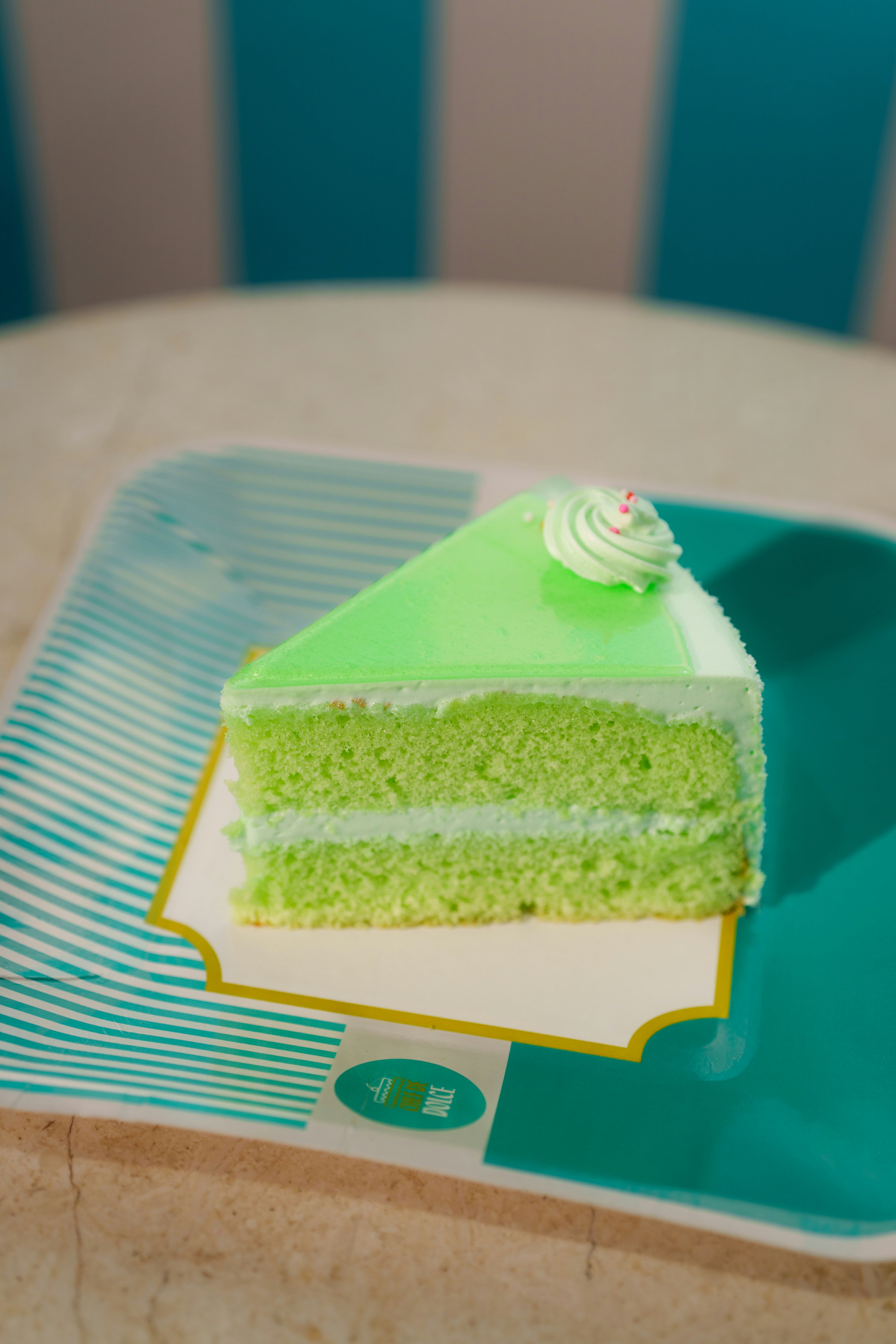 A slice of green layer cake with frosting on a patterned plate