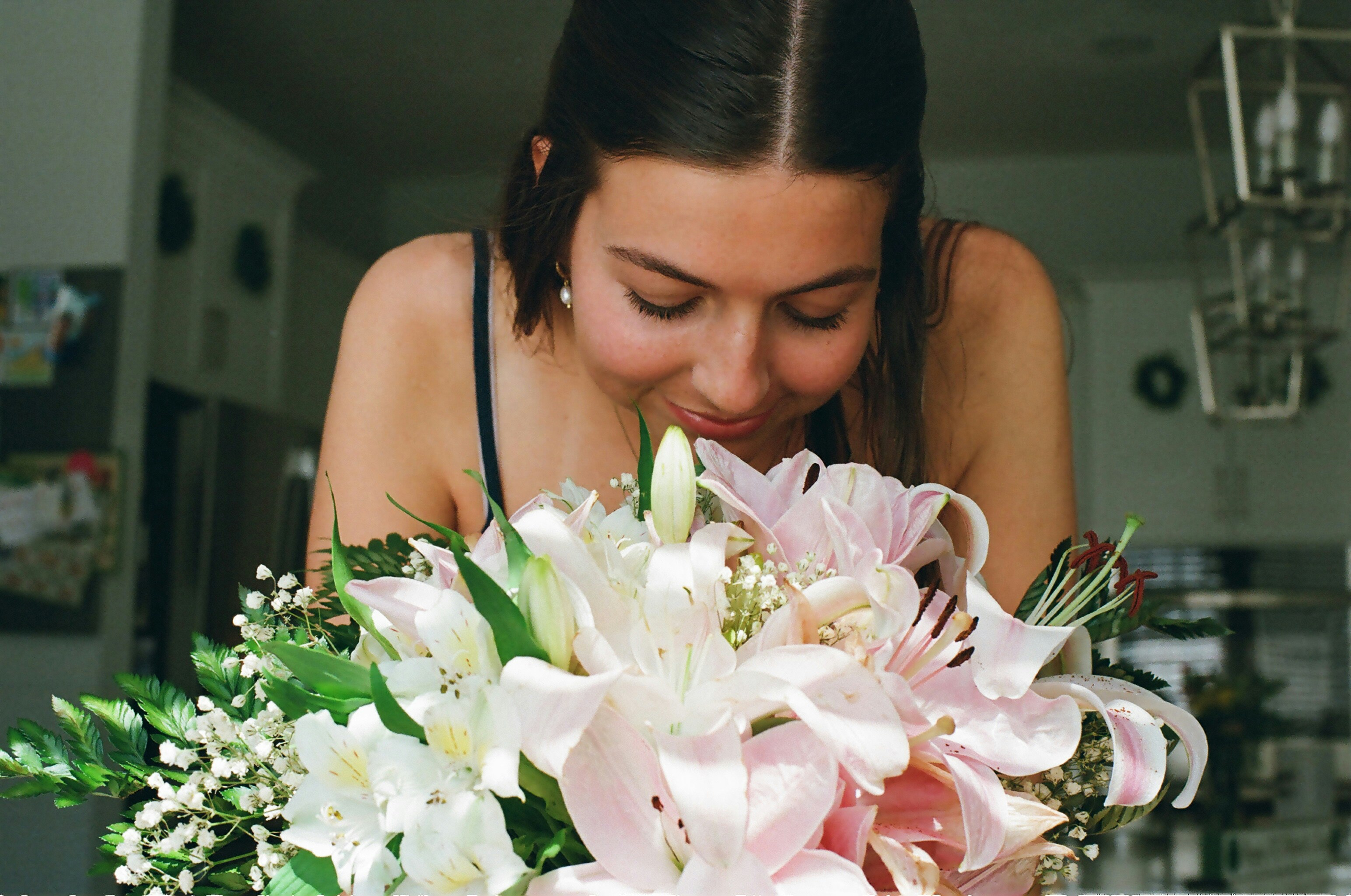 A woman leaning forward to smell a bouquet of pink and white lilies