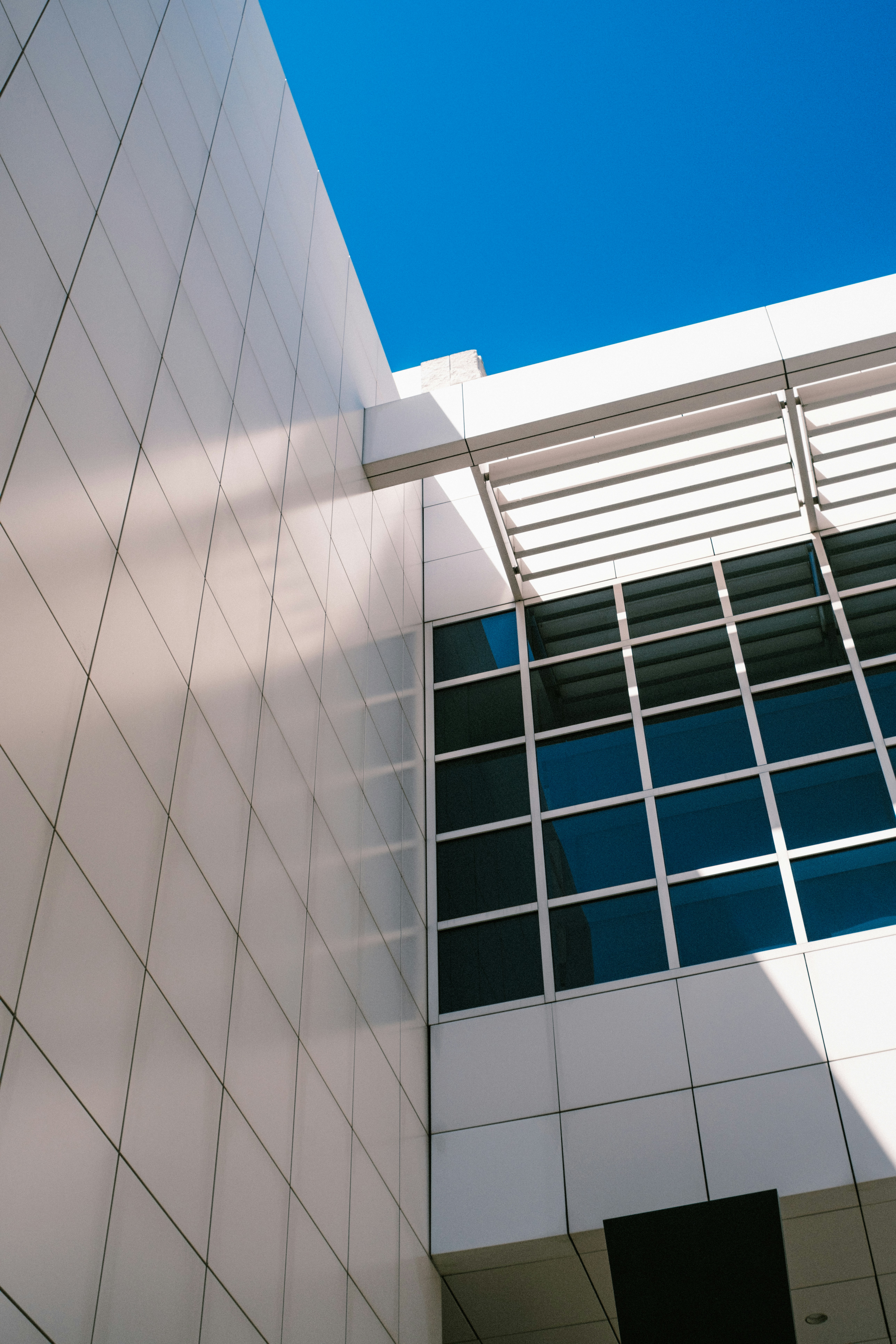 Modern building facade with white square tiles and a glass window under blue sky