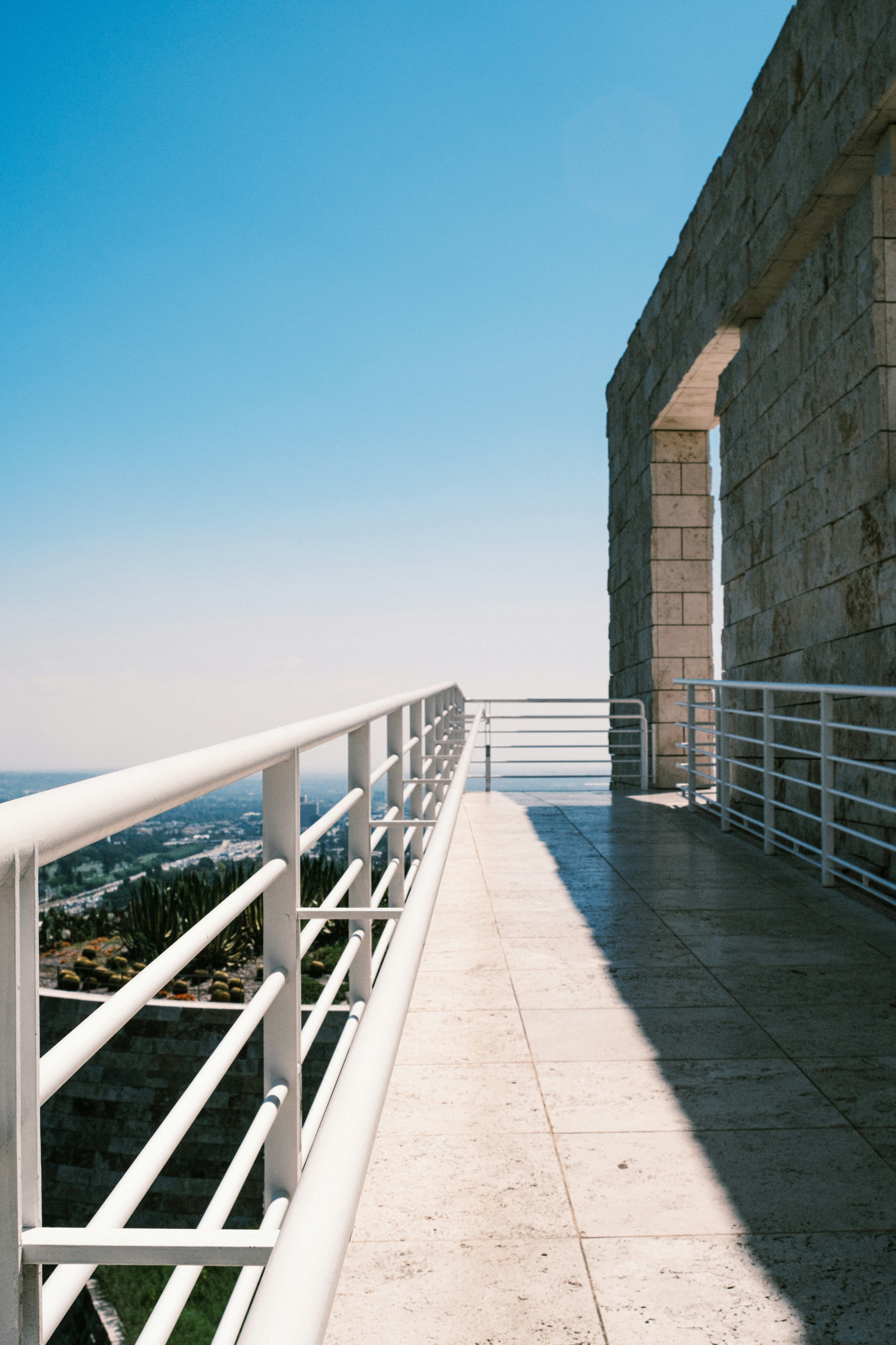 A stone balcony with white railings overlooking a distant city under a clear sky