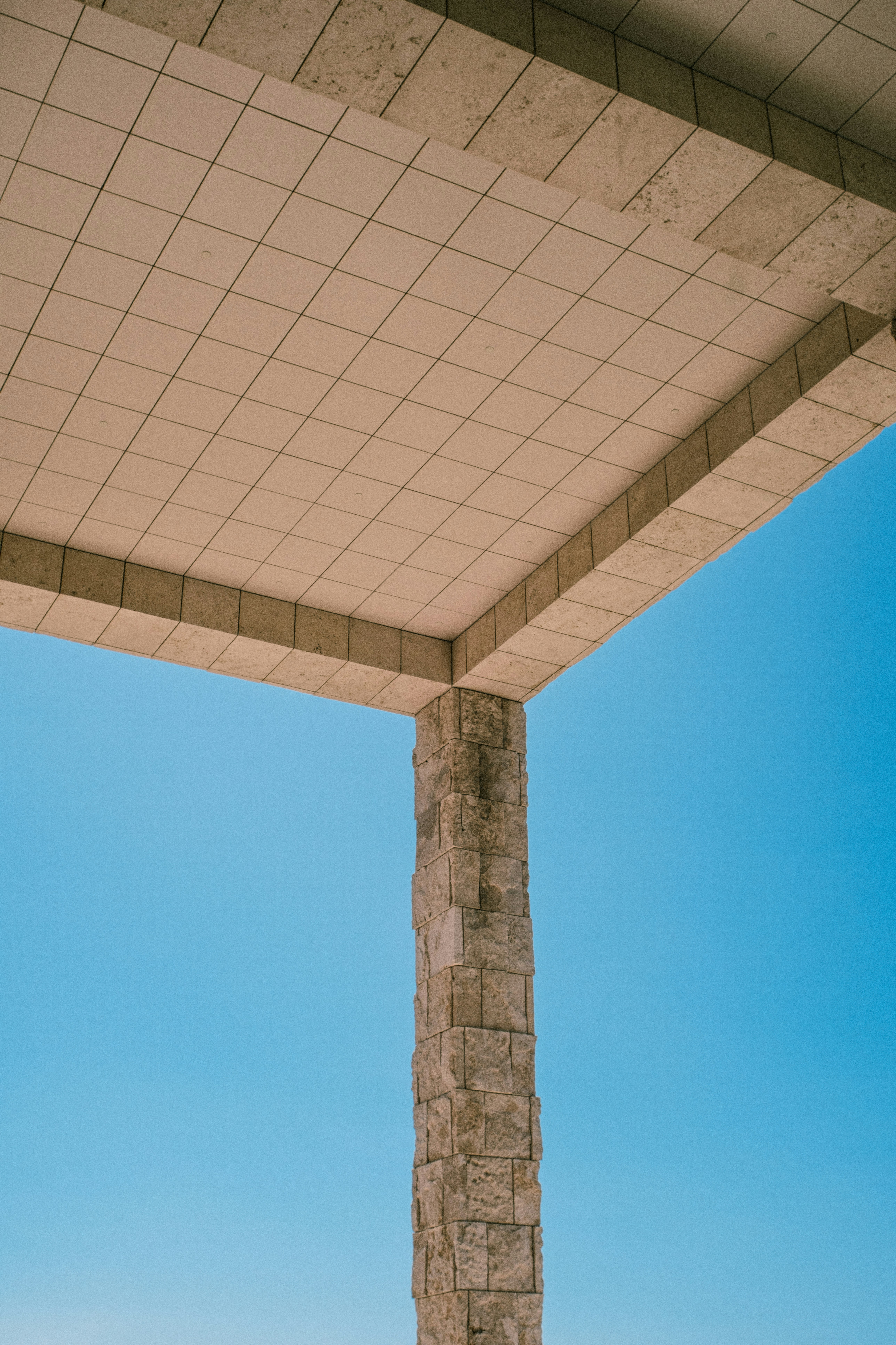 A stone pillar supporting a tiled ceiling against a clear blue sky
