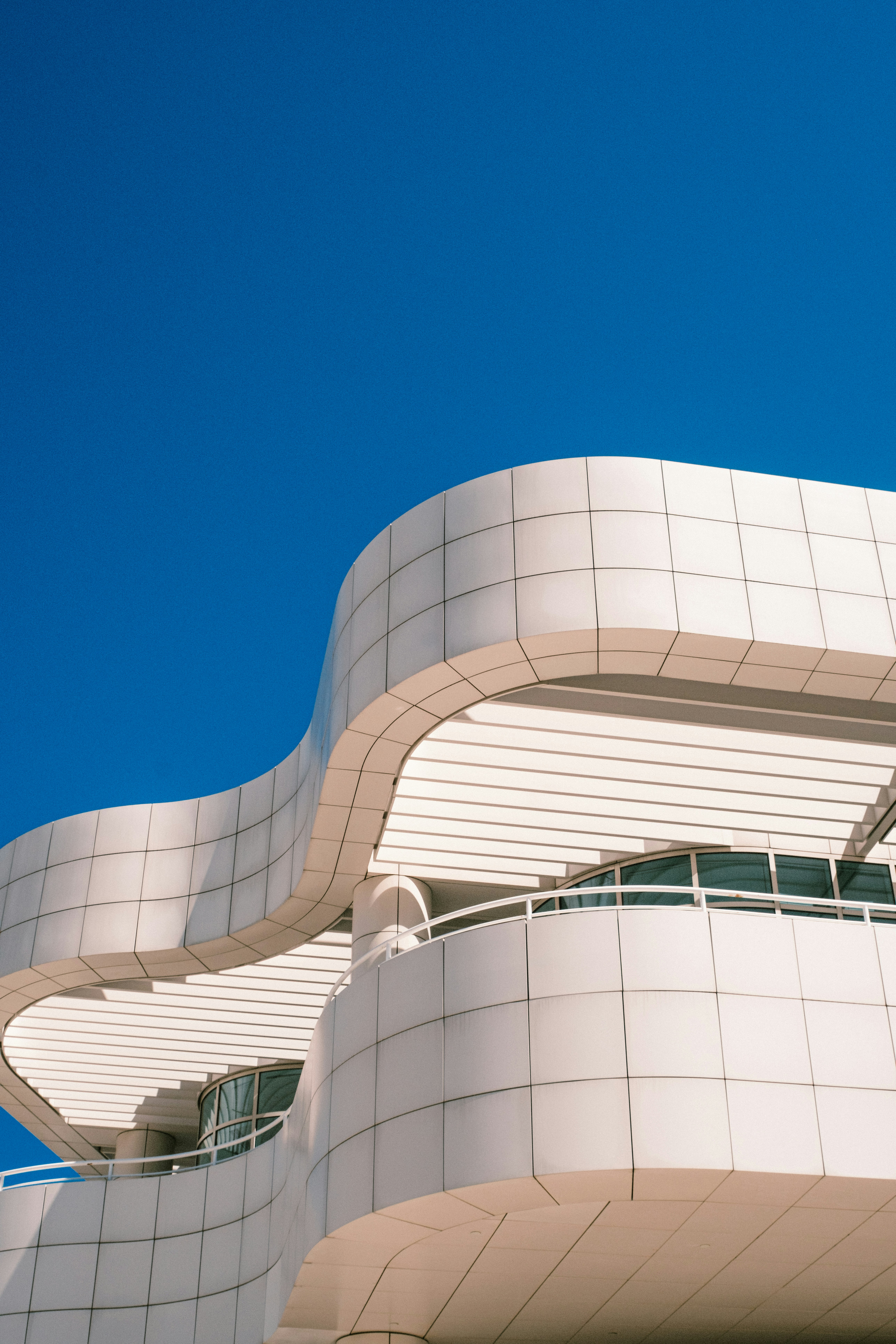 Curved white tiled building facade against a clear deep blue sky