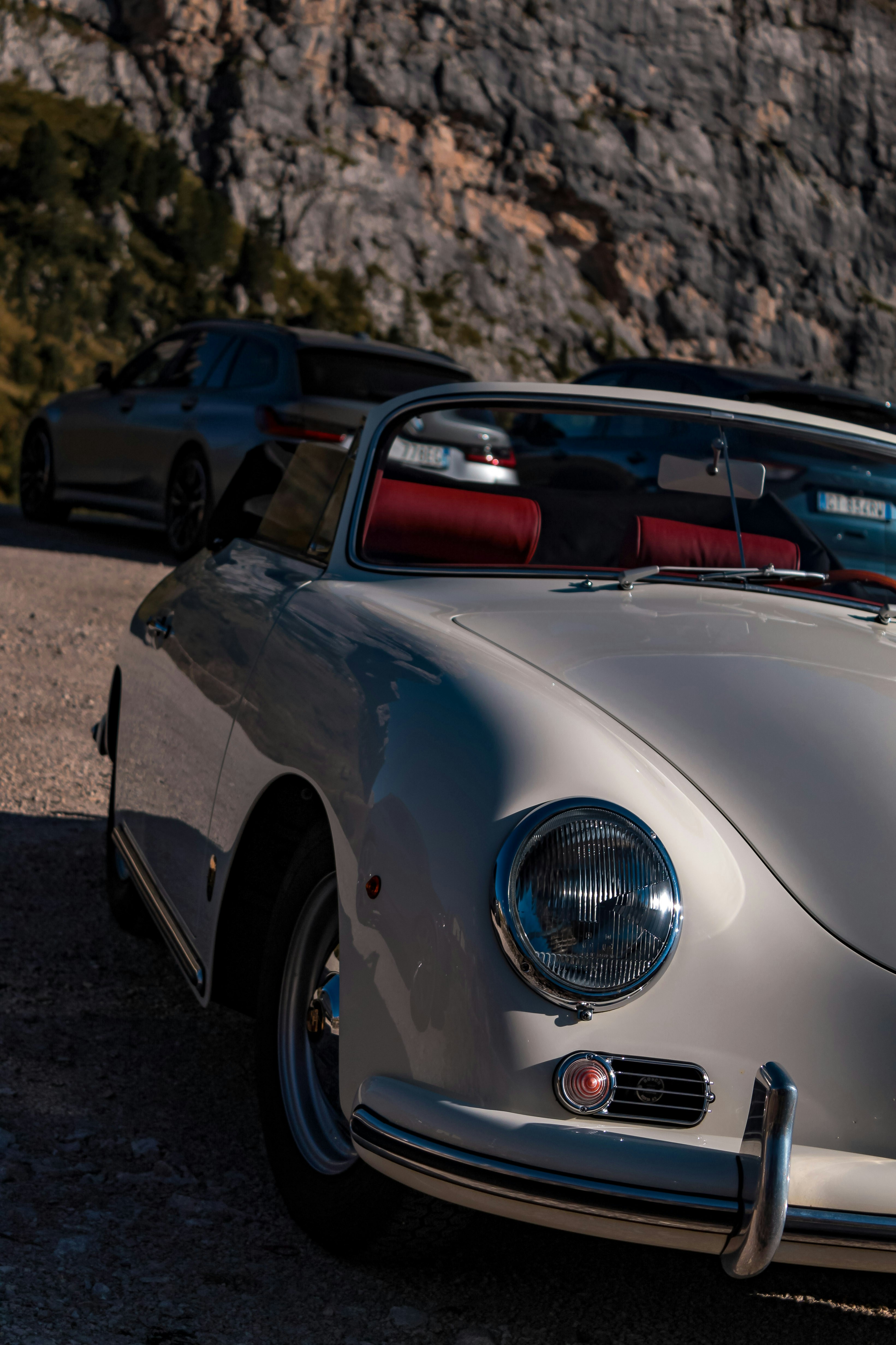 Una cabriolet d'epoca bianca con sedili rossi parcheggiata su una strada di montagna ghiaiosa
