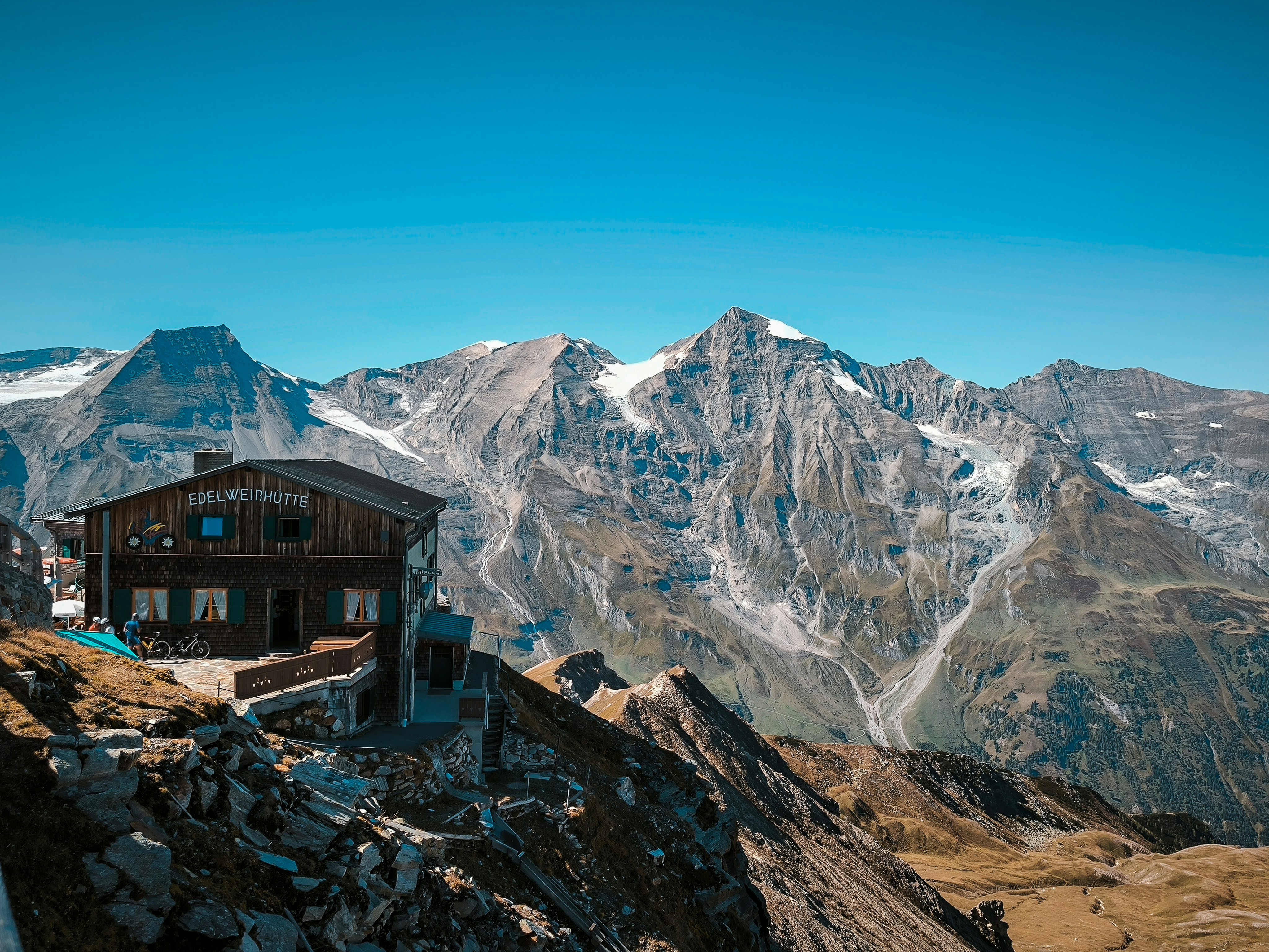 La capanna di montagna Edelweinhütte su una cresta rocciosa davanti a cime innevate sotto un cielo azzurro