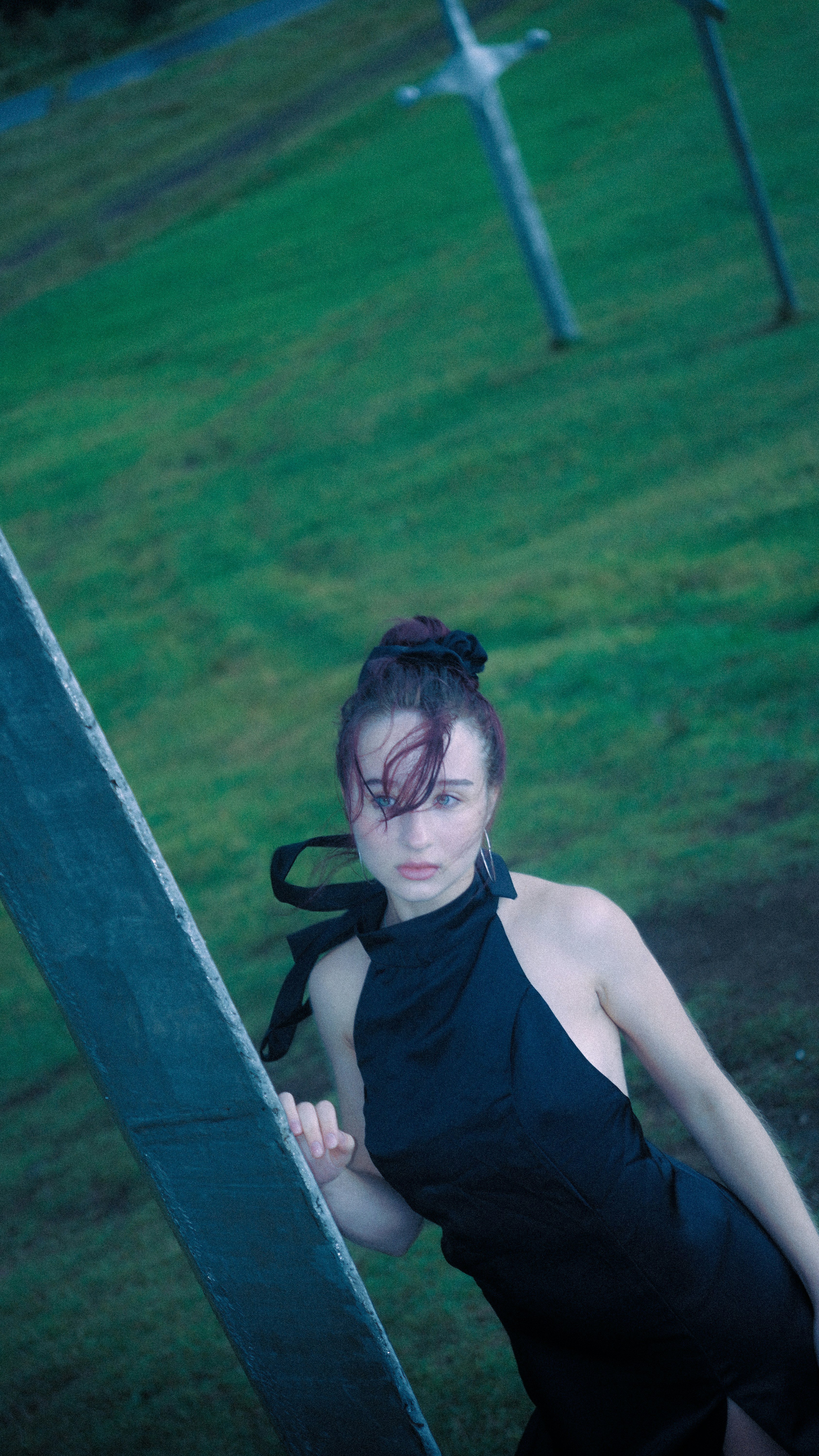 A woman in a black halter dress leaning against a concrete post on grass