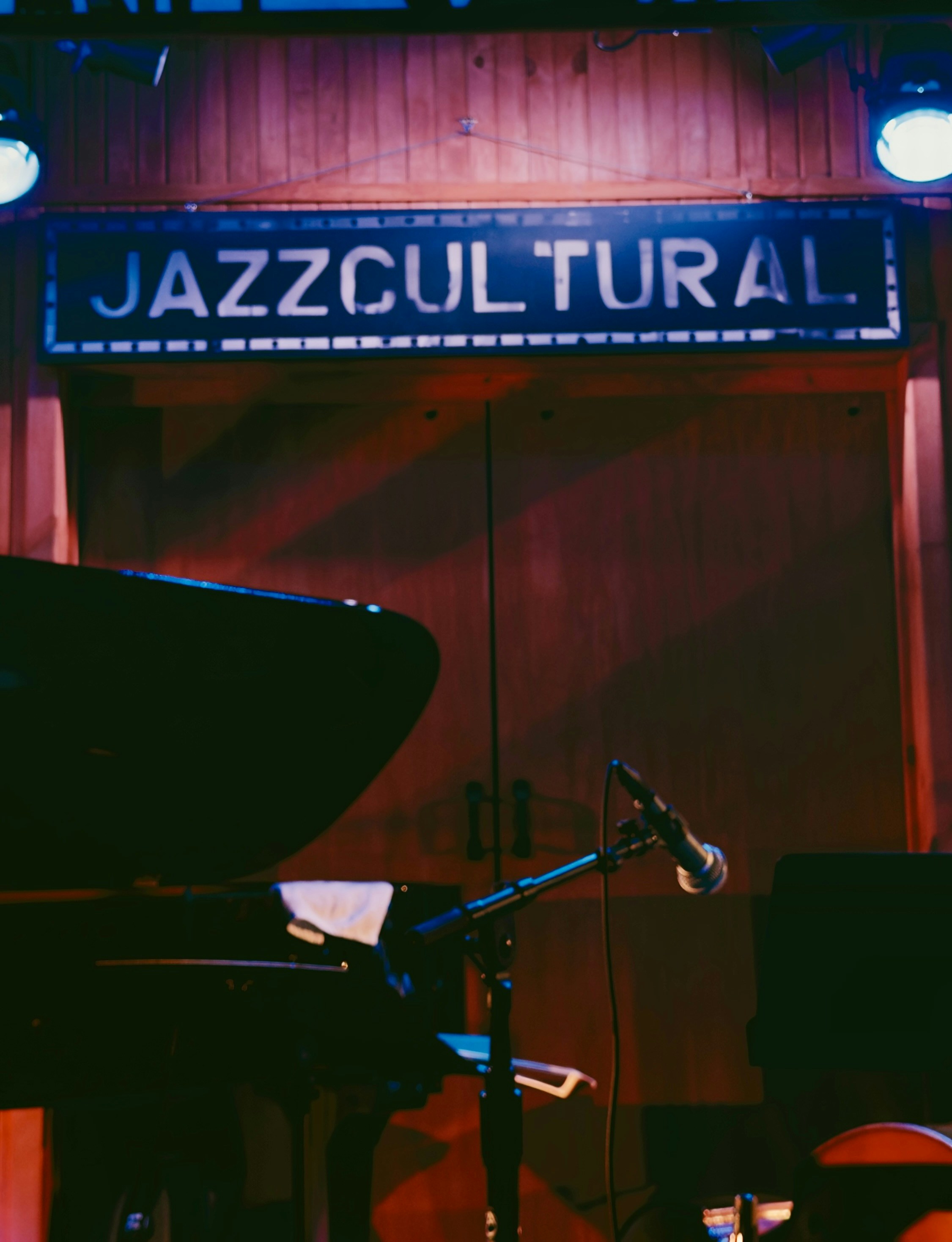 A grand piano and microphone on a stage under a sign reading JAZZCULTURAL
