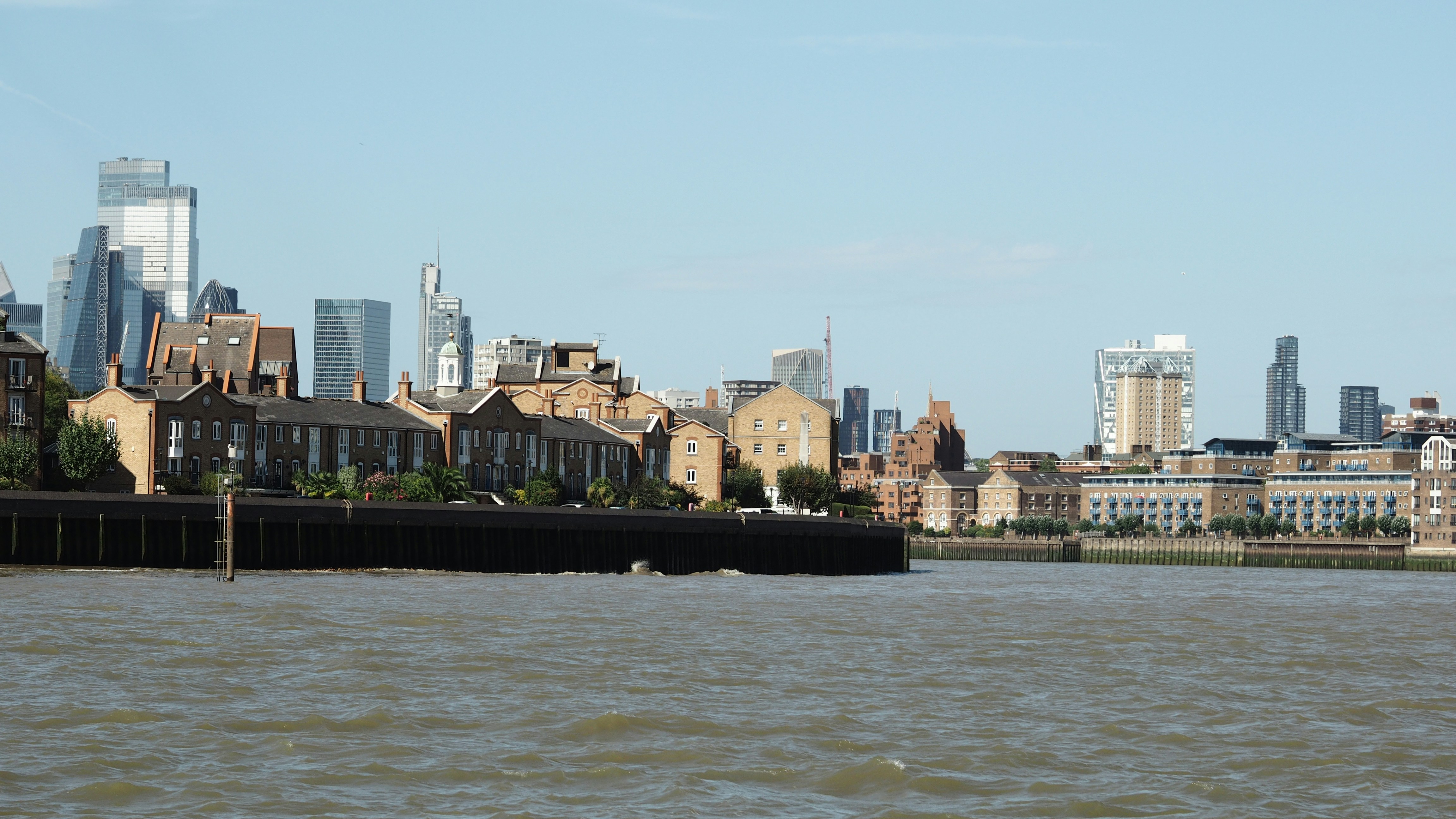 Backsteingebäude entlang des Themseufers mit der Londoner Skyline im Hintergrund