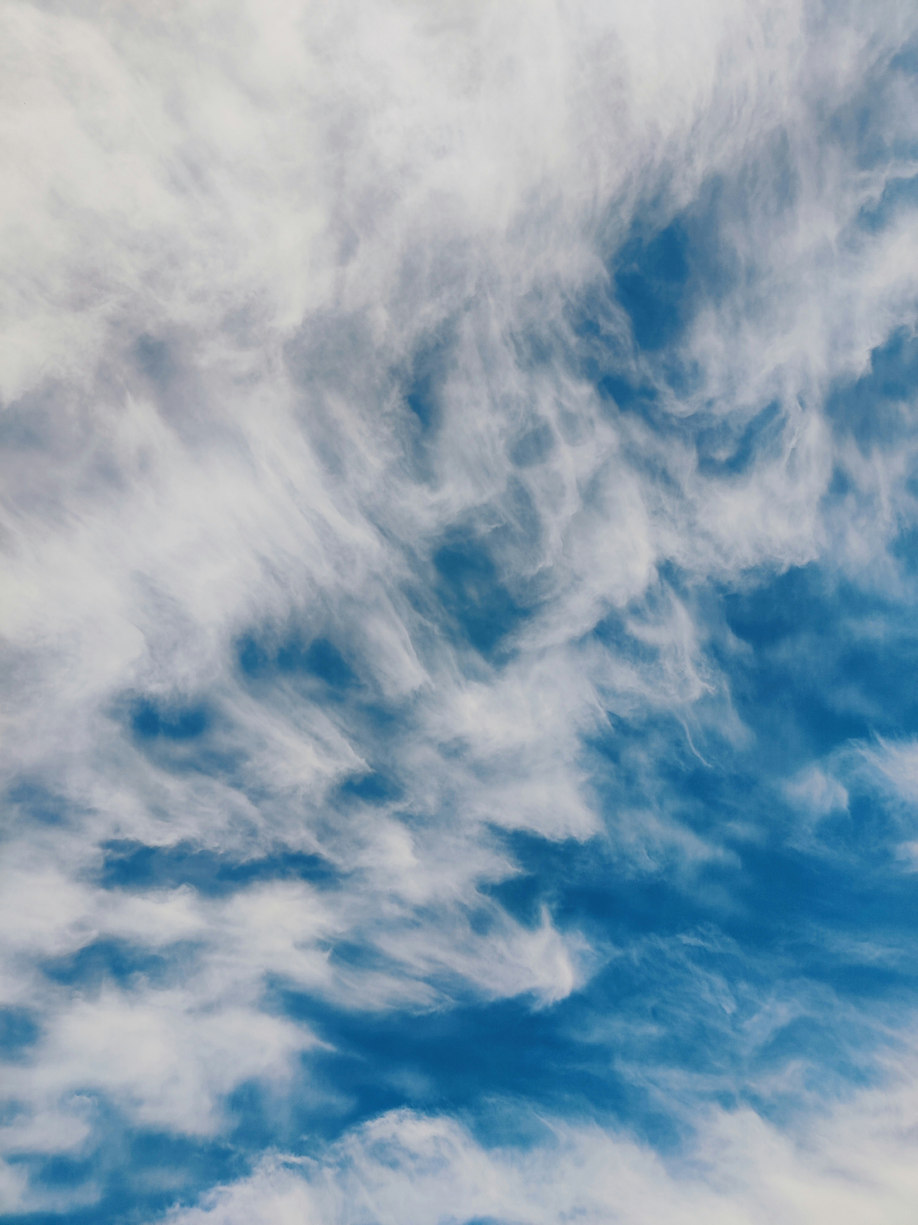 Wispy white cirrus clouds scattered across a bright blue sky