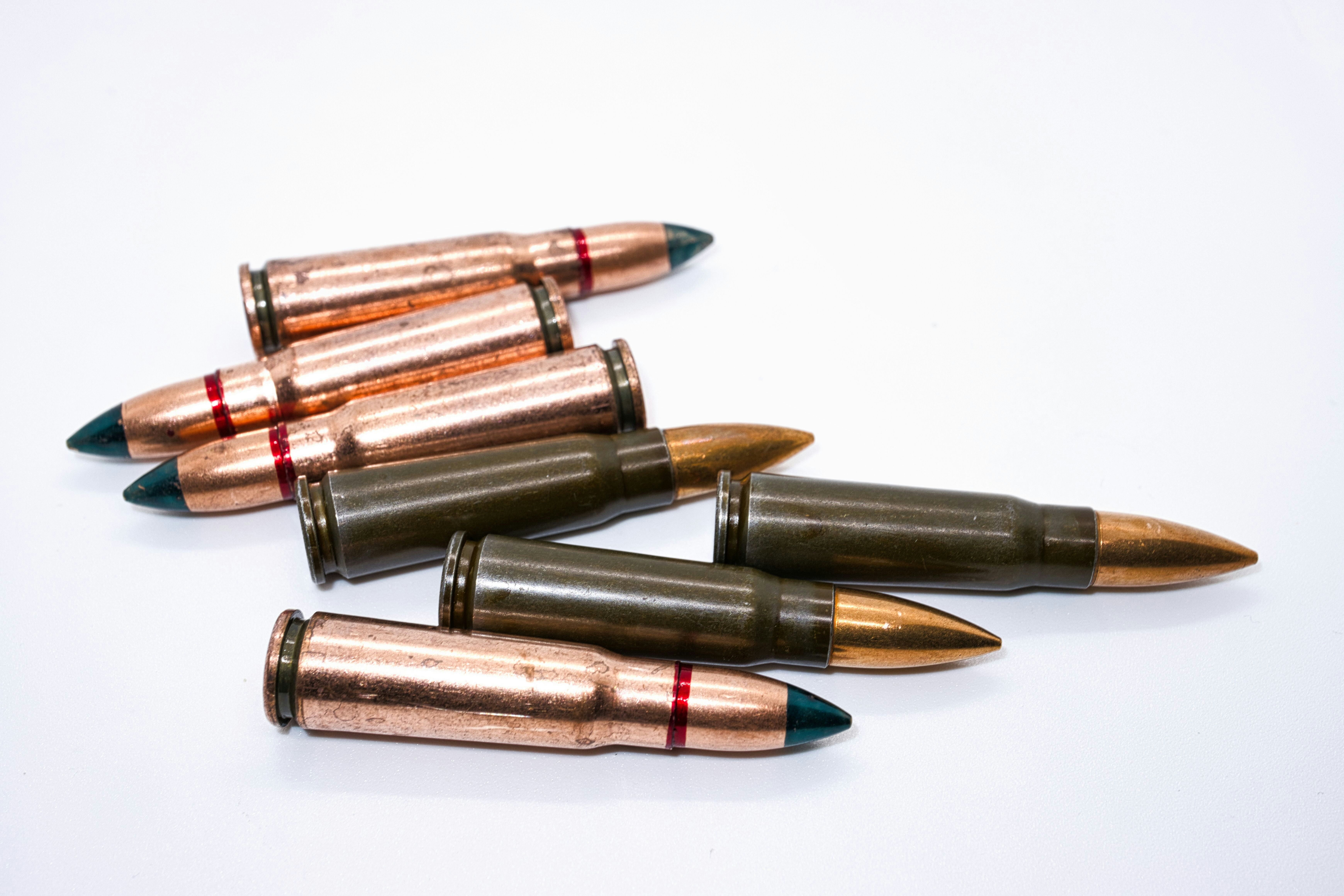 Un tas de cartouches de fusil en cuivre et vert olive sur une surface blanche
