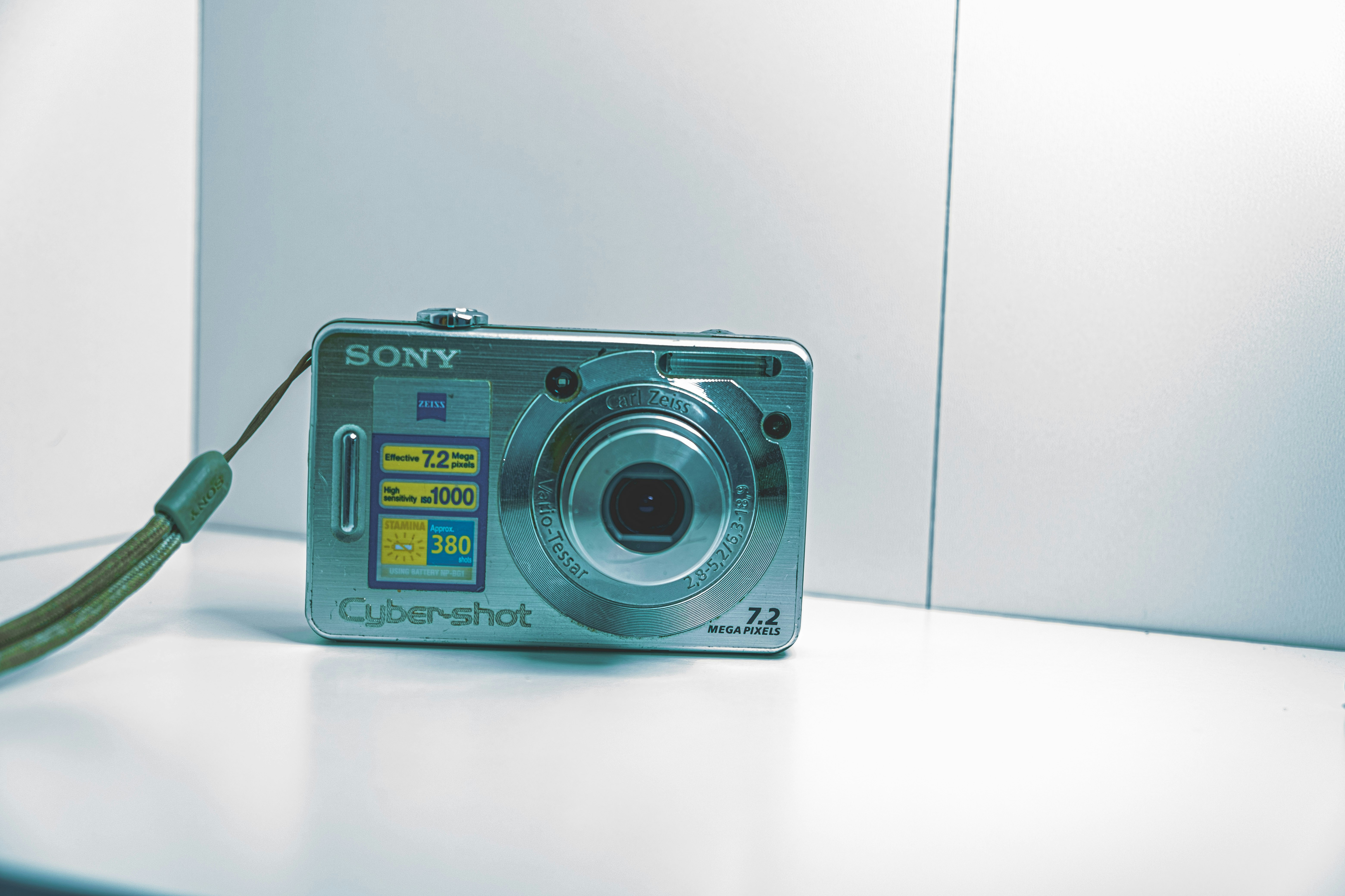 A silver digital camera with a wrist strap on a white surface