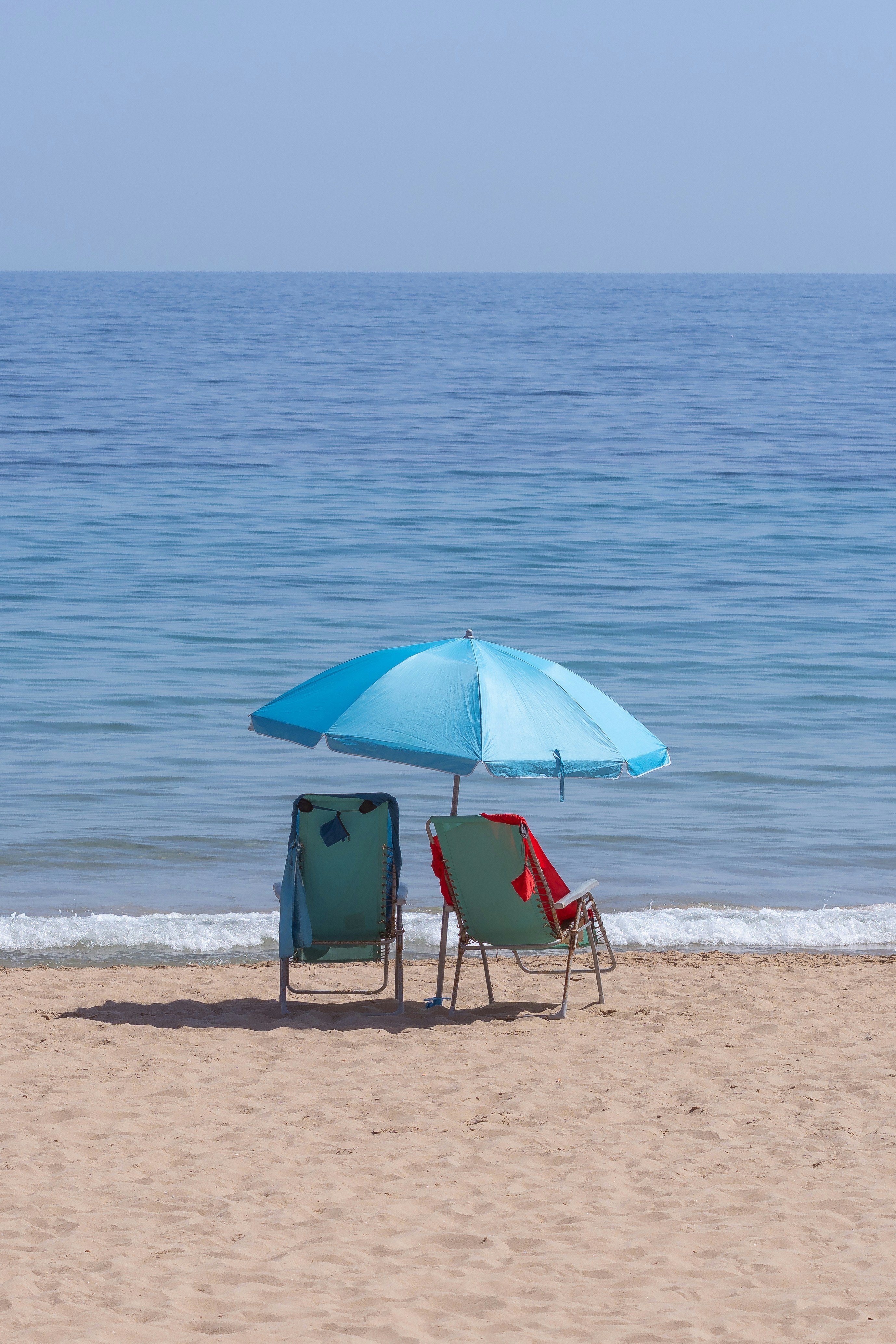 Two beach chairs under a blue umbrella on the sand by the ocean