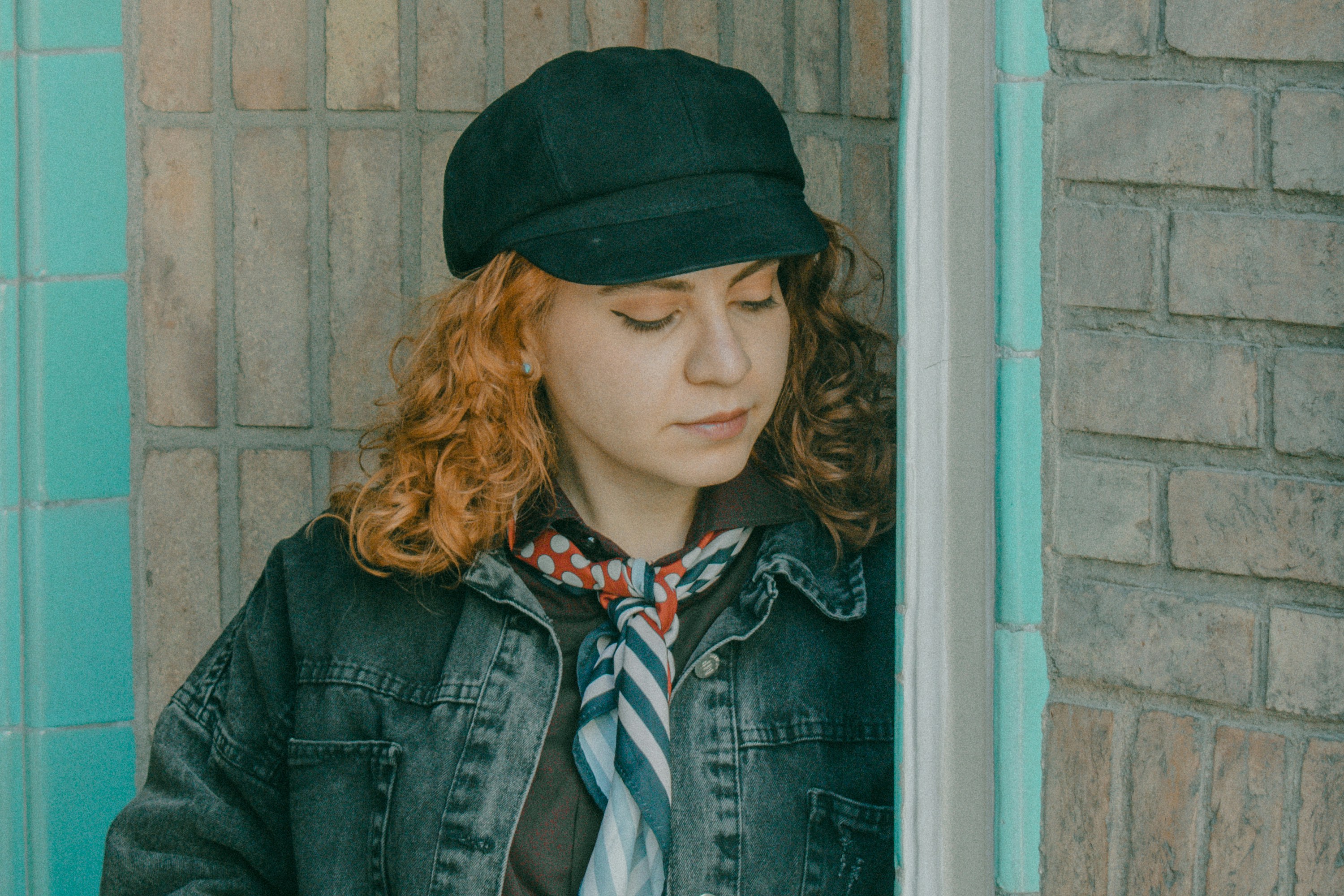 A woman with curly red hair wearing a black cap and denim jacket