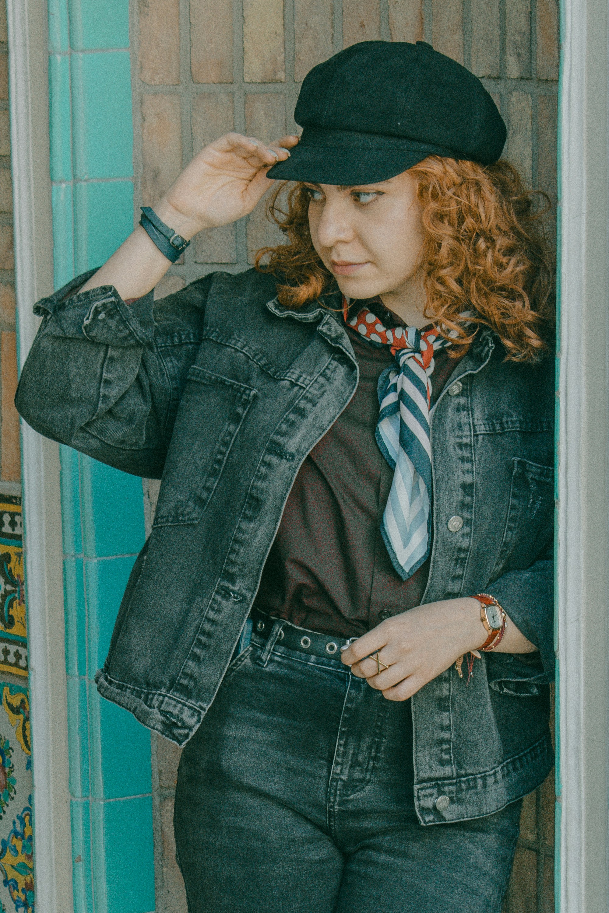 A woman with curly red hair wearing a black cap and denim jacket