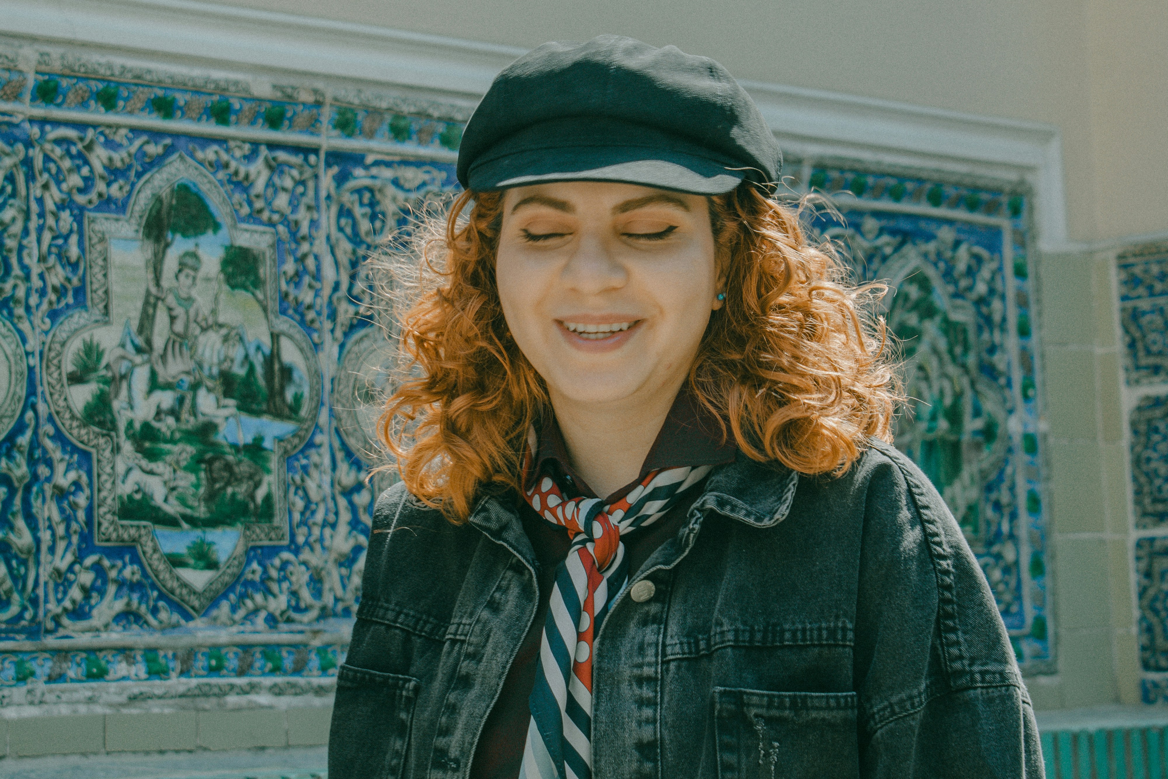 A woman with curly red hair wearing a black cap and denim jacket