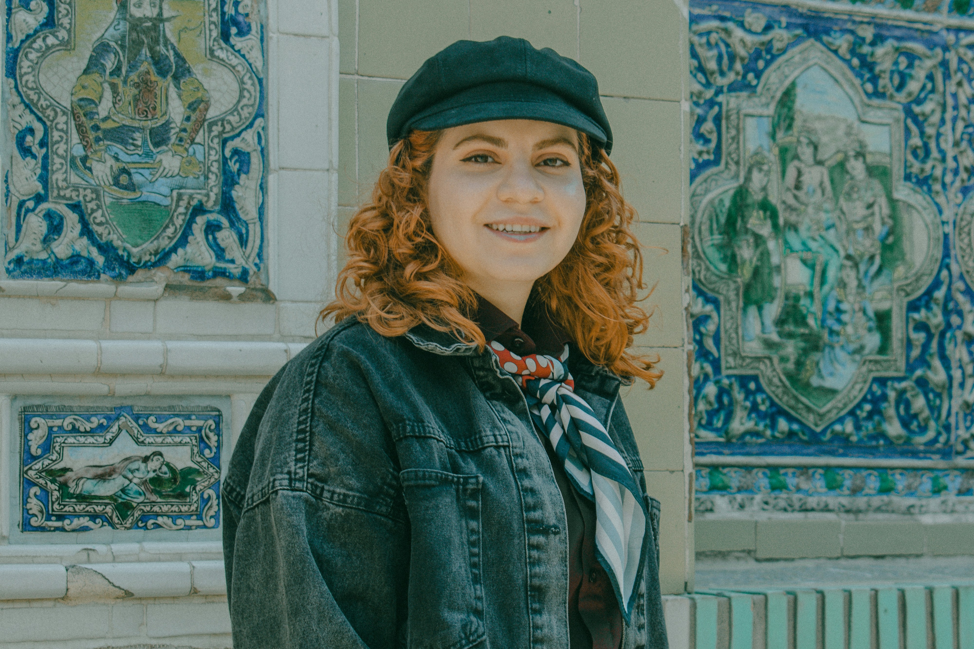 A woman with curly red hair wearing a black cap and denim jacket